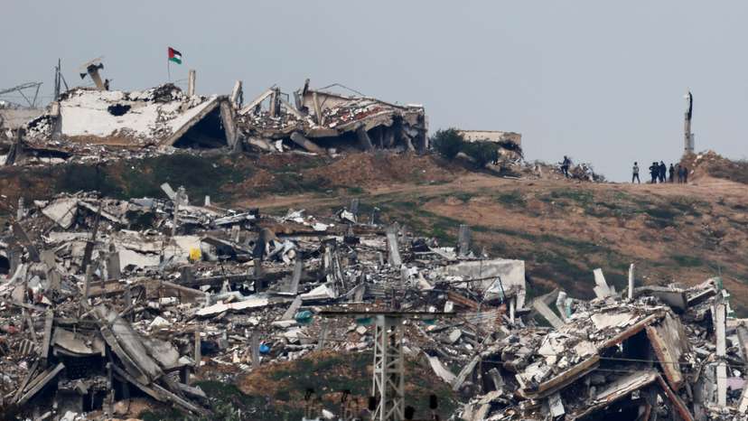 Palestinian flag flutters as people walk near buildings in ruins in Gaza, as seen from Israel