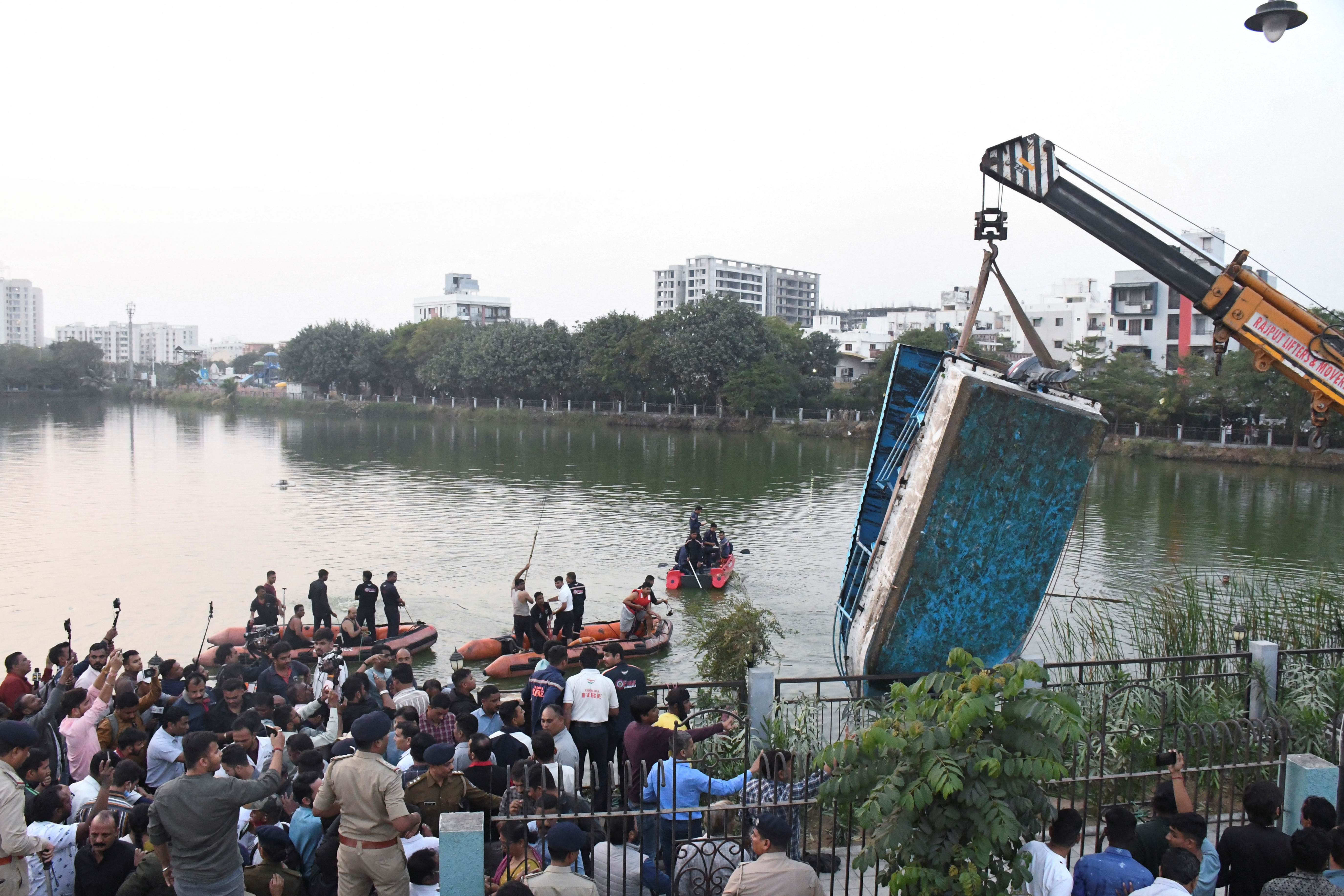 A crane pulls out a boat which capsized carrying children and teachers who were on a picnic in Harni Lake in Vadodara