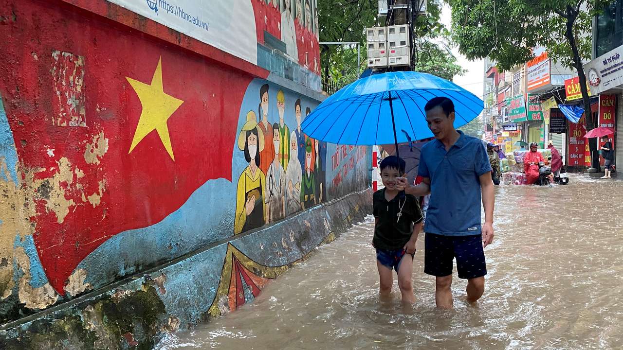 A man and a boy walk through a flooded street after heavy rains in Hanoi