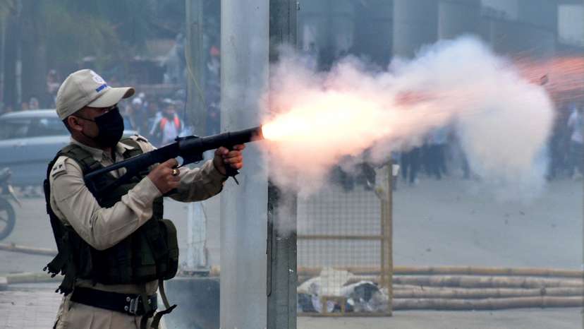 A police officer fires a tear smoke shell to disperse demonstrators during a protest march, in Imphal