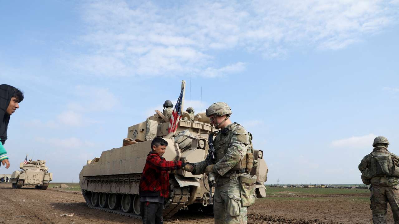 FILE PHOTO: A soldier from the US-led coalition holds the hand of a boy in the countryside of Qamishli