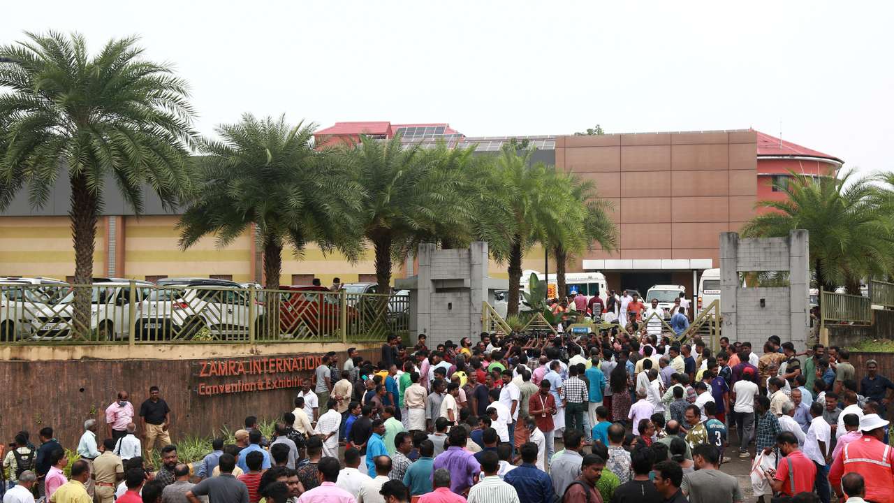People stand outside a convention centre where multiple blasts occurred during a religious gathering in Kochi