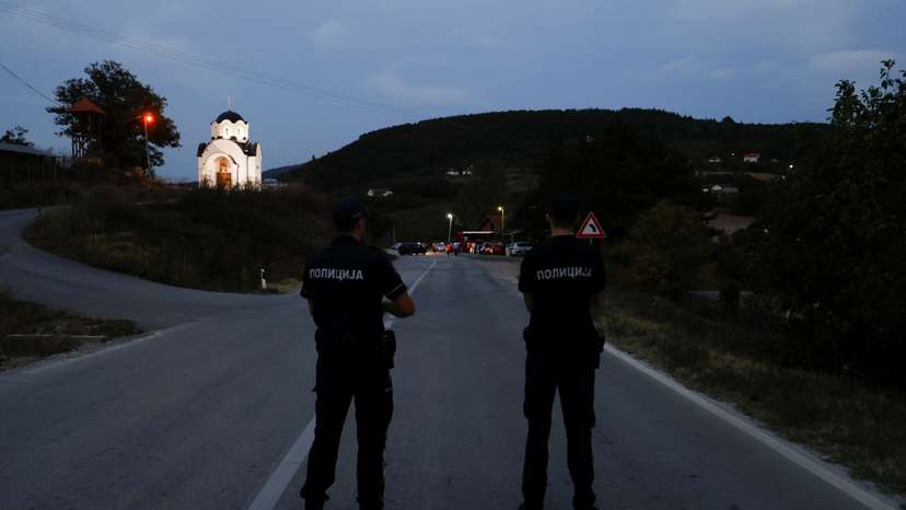 Police officers stand guard as protestors partially block the road near the main Kosovo-Serbia border crossing in Merdare