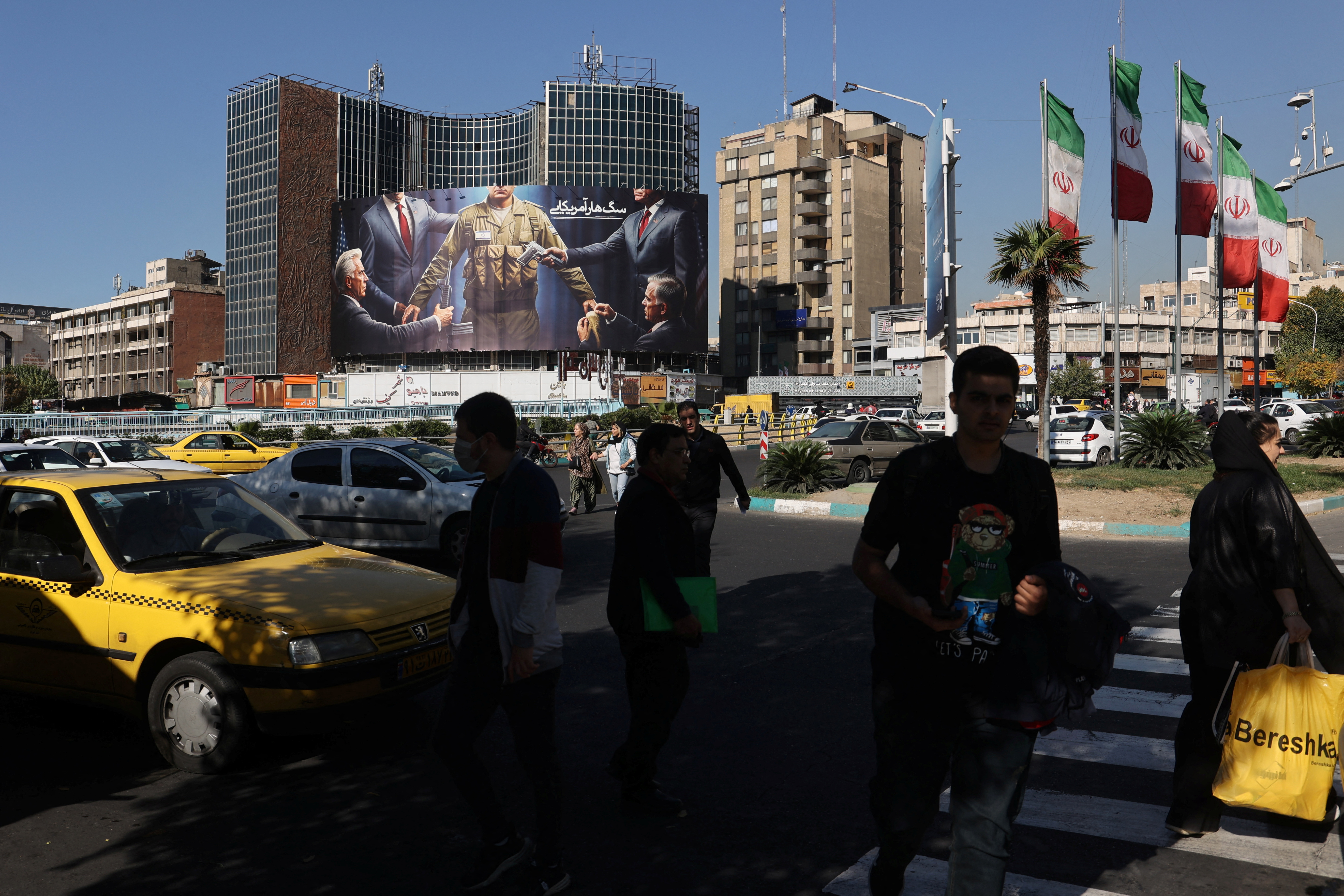 Iranians walk next to a billboard on a street in Tehran
