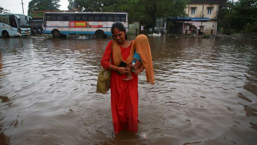 A woman carries her son, covered with a scarf, through a water-logged bus terminal as it rains in Kochi