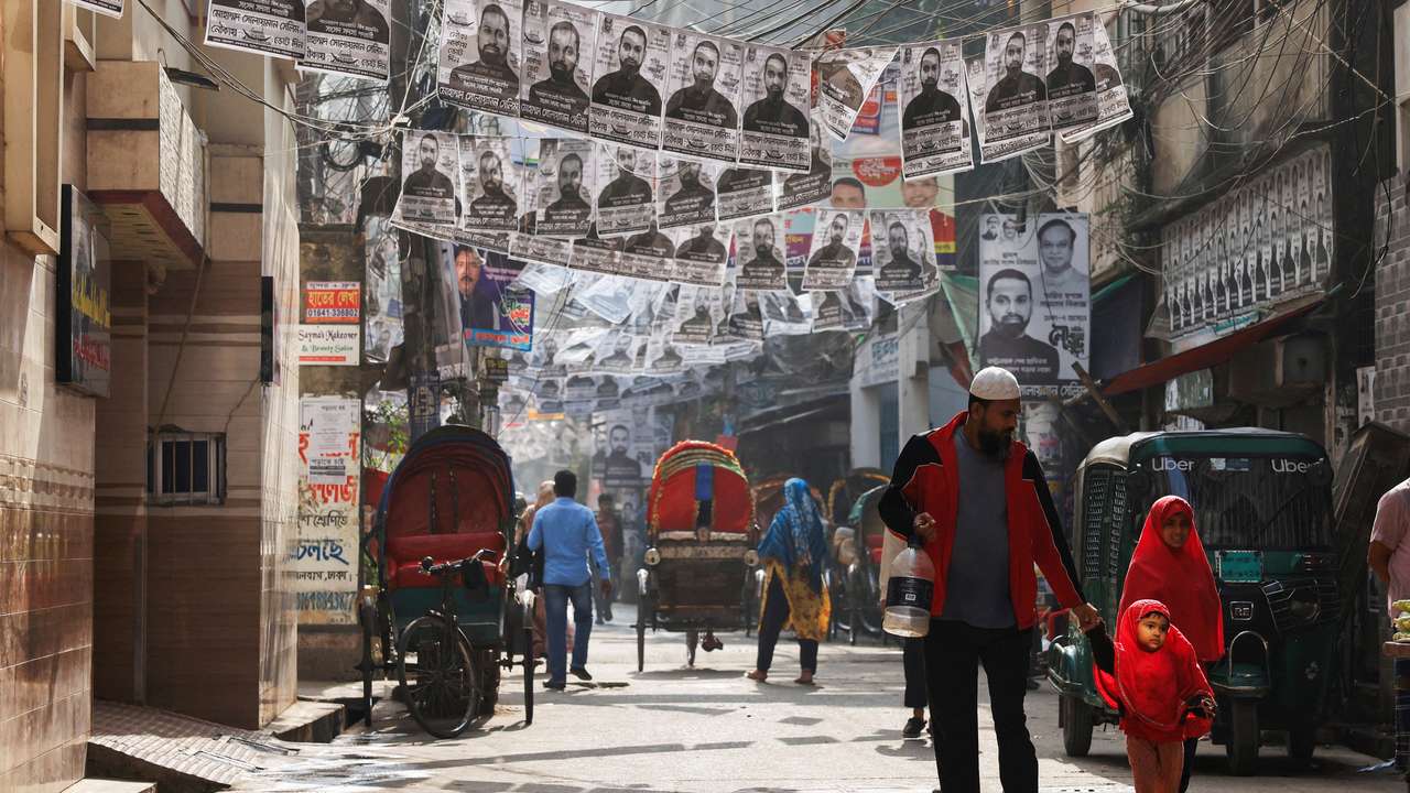 FILE PHOTO: Commuters pass by as posters of an election candidate hang on the street ahead of the general election in Dhaka
