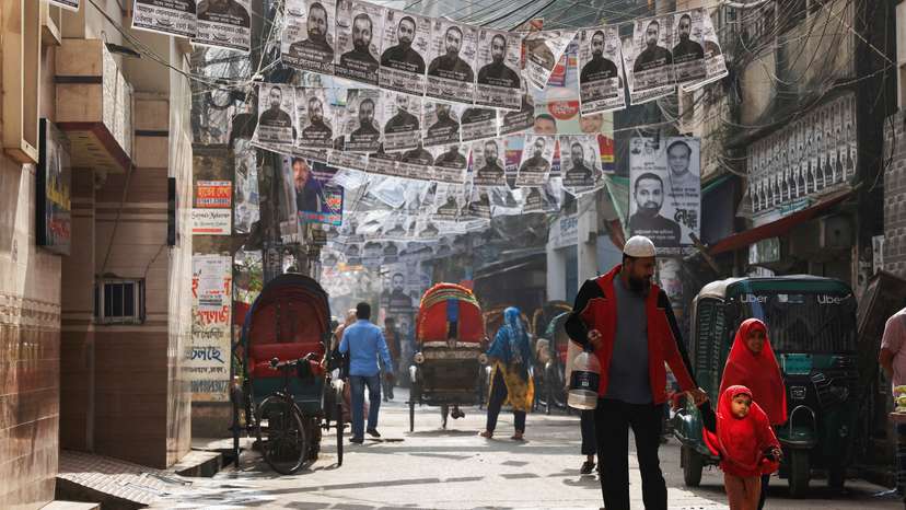 FILE PHOTO: Commuters pass by as posters of an election candidate hang on the street ahead of the general election in Dhaka