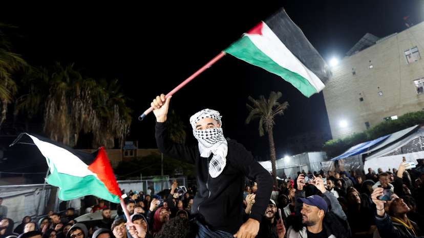A man waves Palestinian flags as Palestinians react to news on a ceasefire deal with Israel, in Deir Al-Balah in the central Gaza Strip