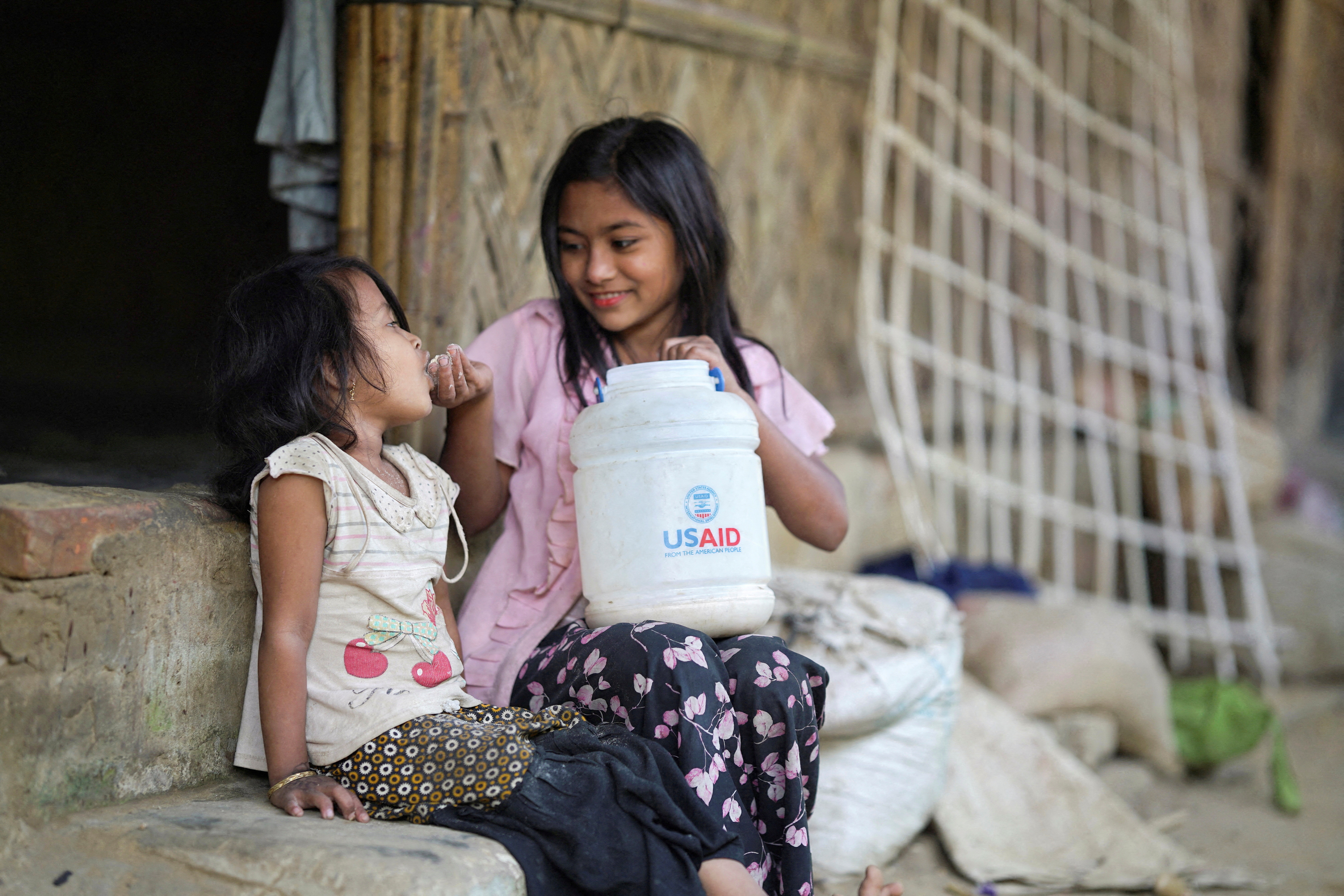 FILE PHOTO: A Rohingya girl feeds a child from a jar with the USAID logo on it at a refugee camp in Cox's Bazar