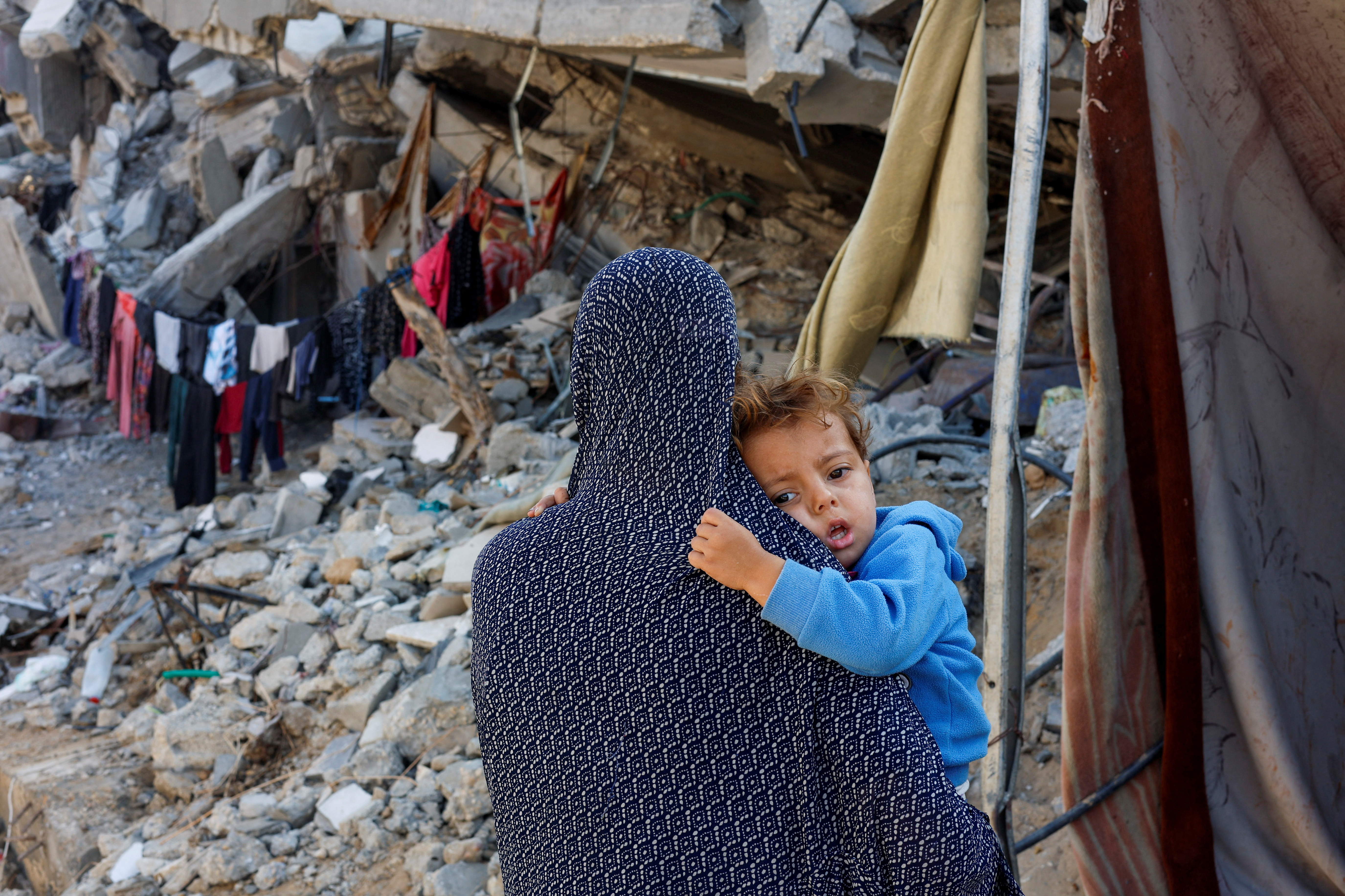 Palestinian woman carries her child near the ruins of a house destroyed in the Israeli military offensive, in Khan Younis in the southern Gaza Strip