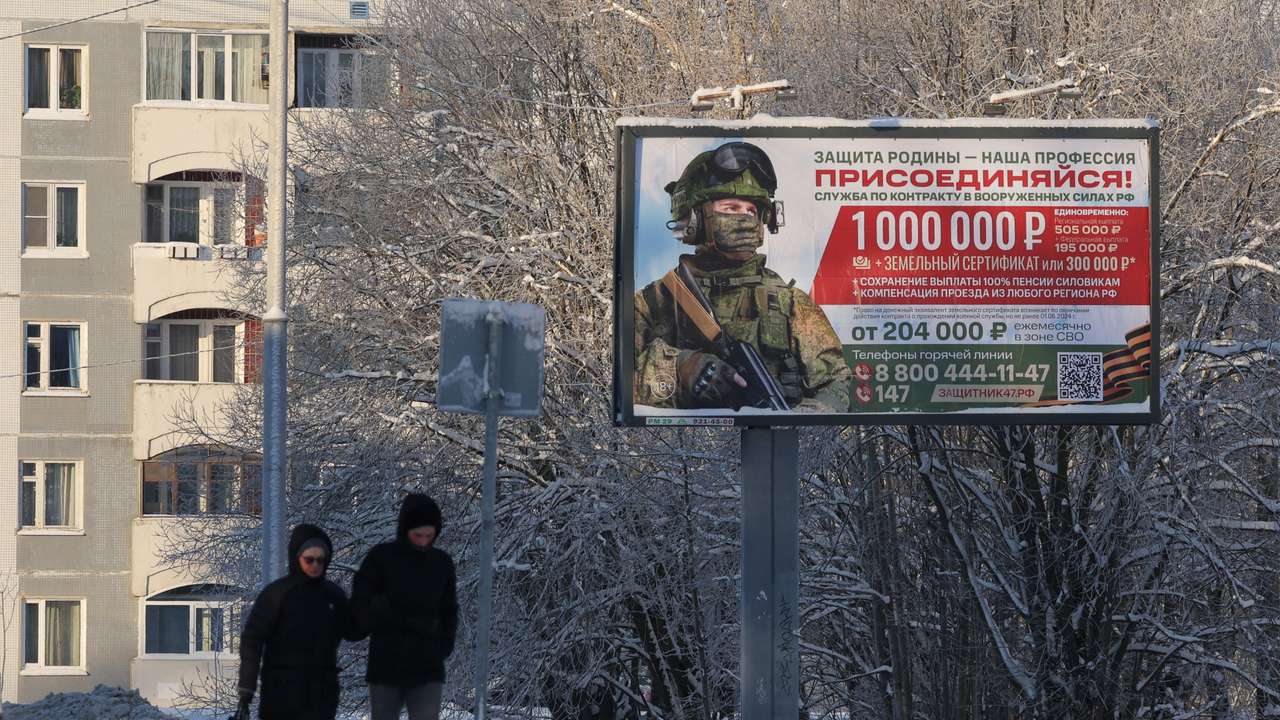 People walk along a street past a billboard promoting military service under the contract in Russian Armed Forces in the town of Gatchina