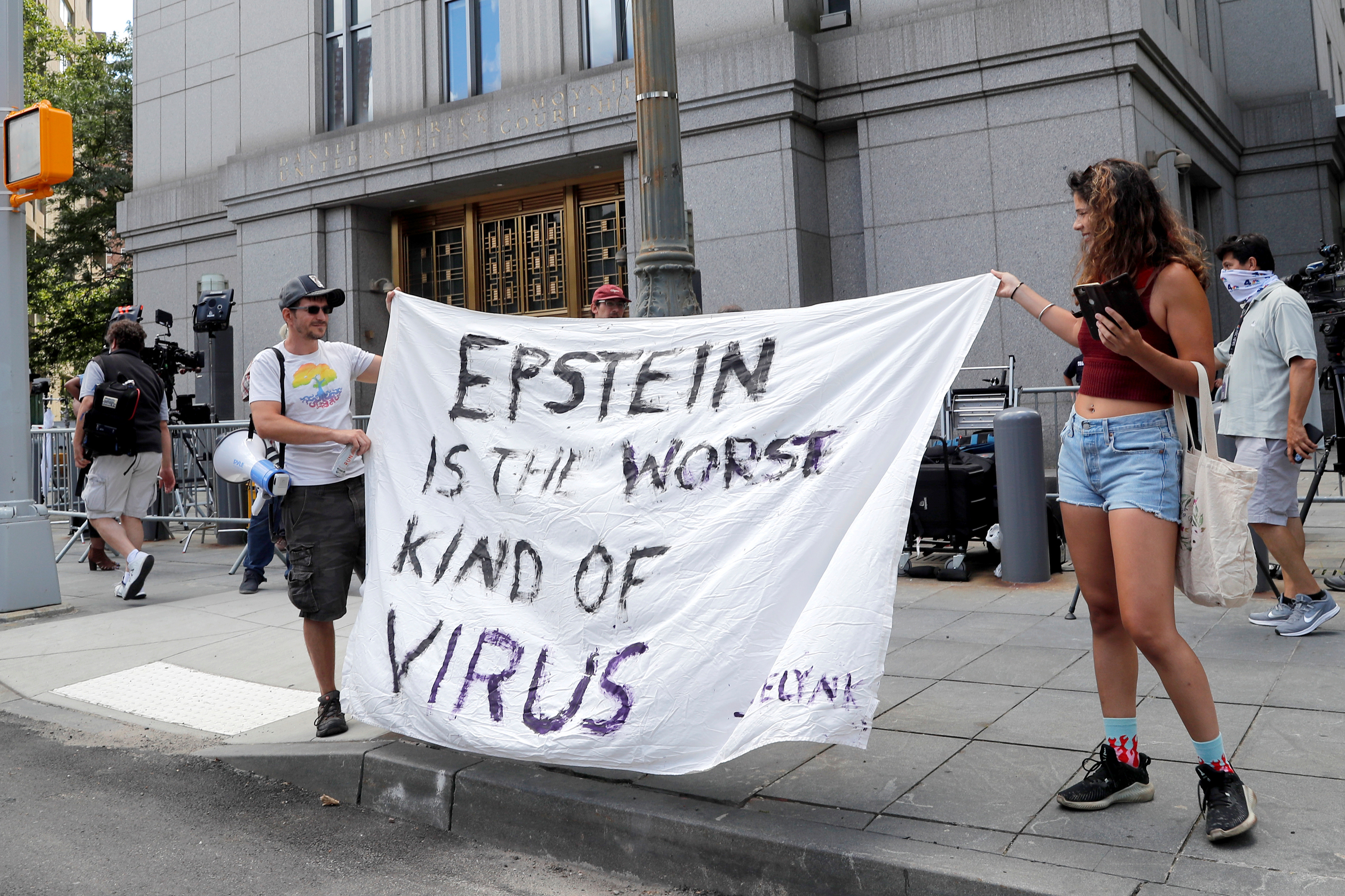 Protesters and members of the news media gather outside Manhattan Federal Court, during the arraignment hearing of Ghislaine Maxwell, in New York