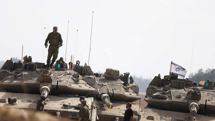 Israeli soliders stand next tanks parked near the Israel-Gaza border, on the Israeli side