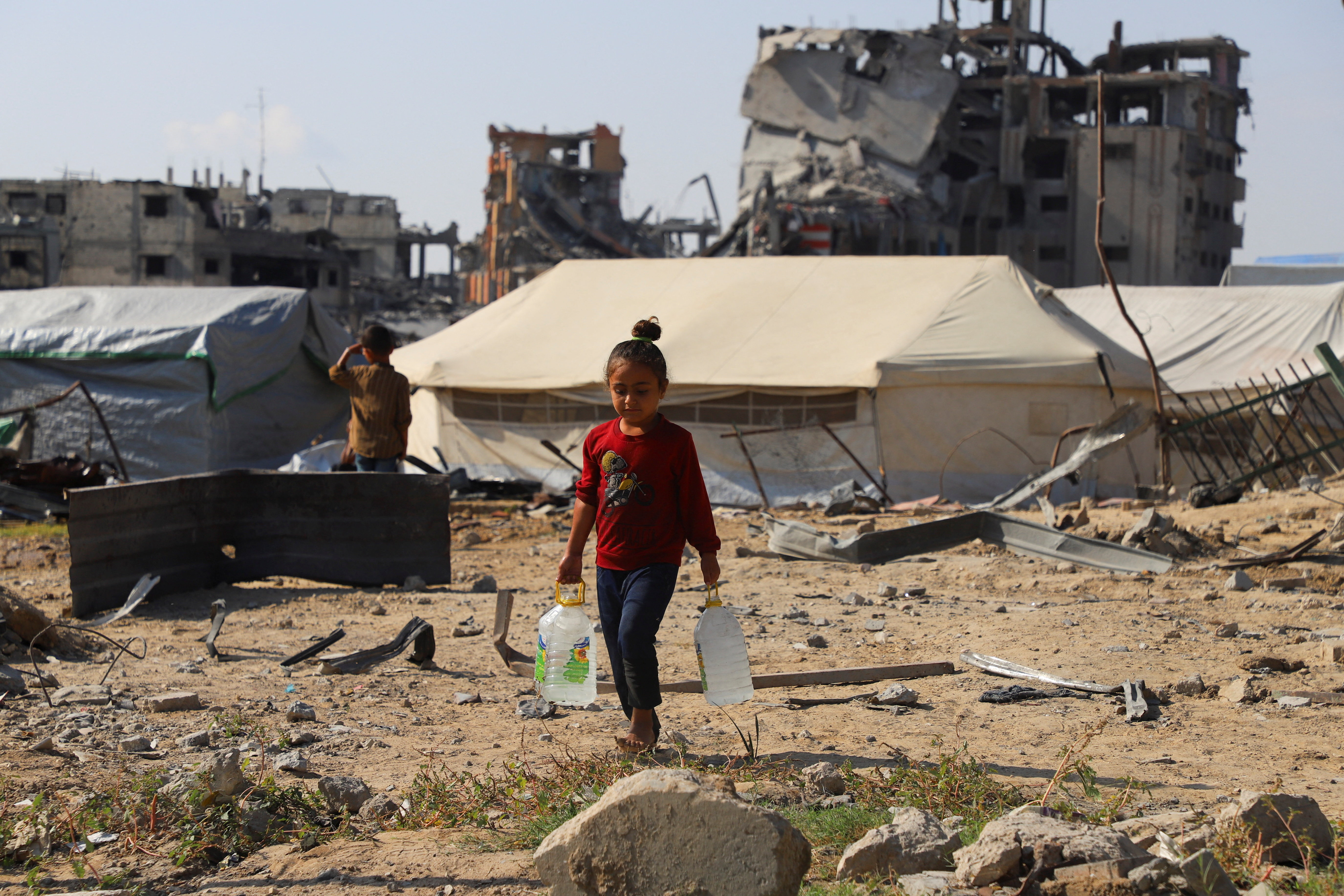 Displaced Palestinian girl carries water containers near tents, amid a ceasefire between Israel and Hamas, in Gaza City