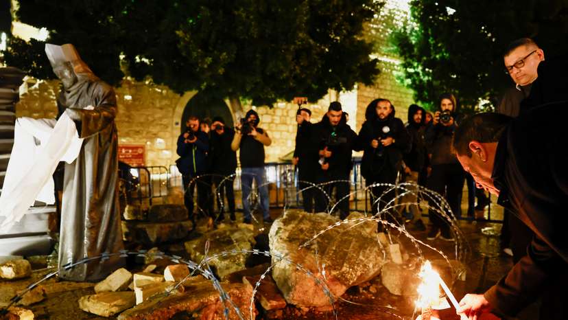 Christmas installation of a grotto with figures standing amid rubble, on Manger Square in Bethlehem