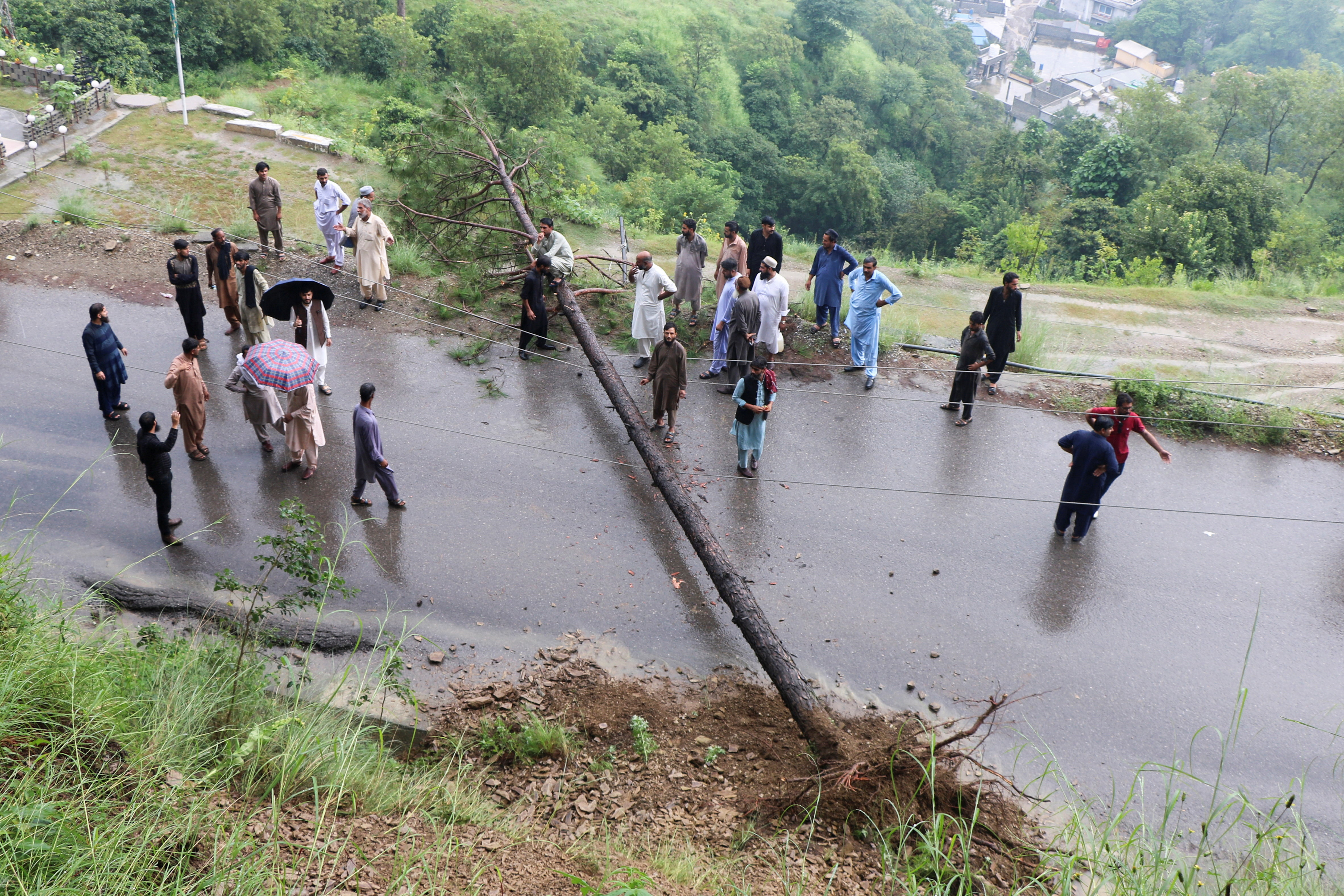Residents gather after a road was blocked by a fallen tree amid heavy rains in Muzaffarabad