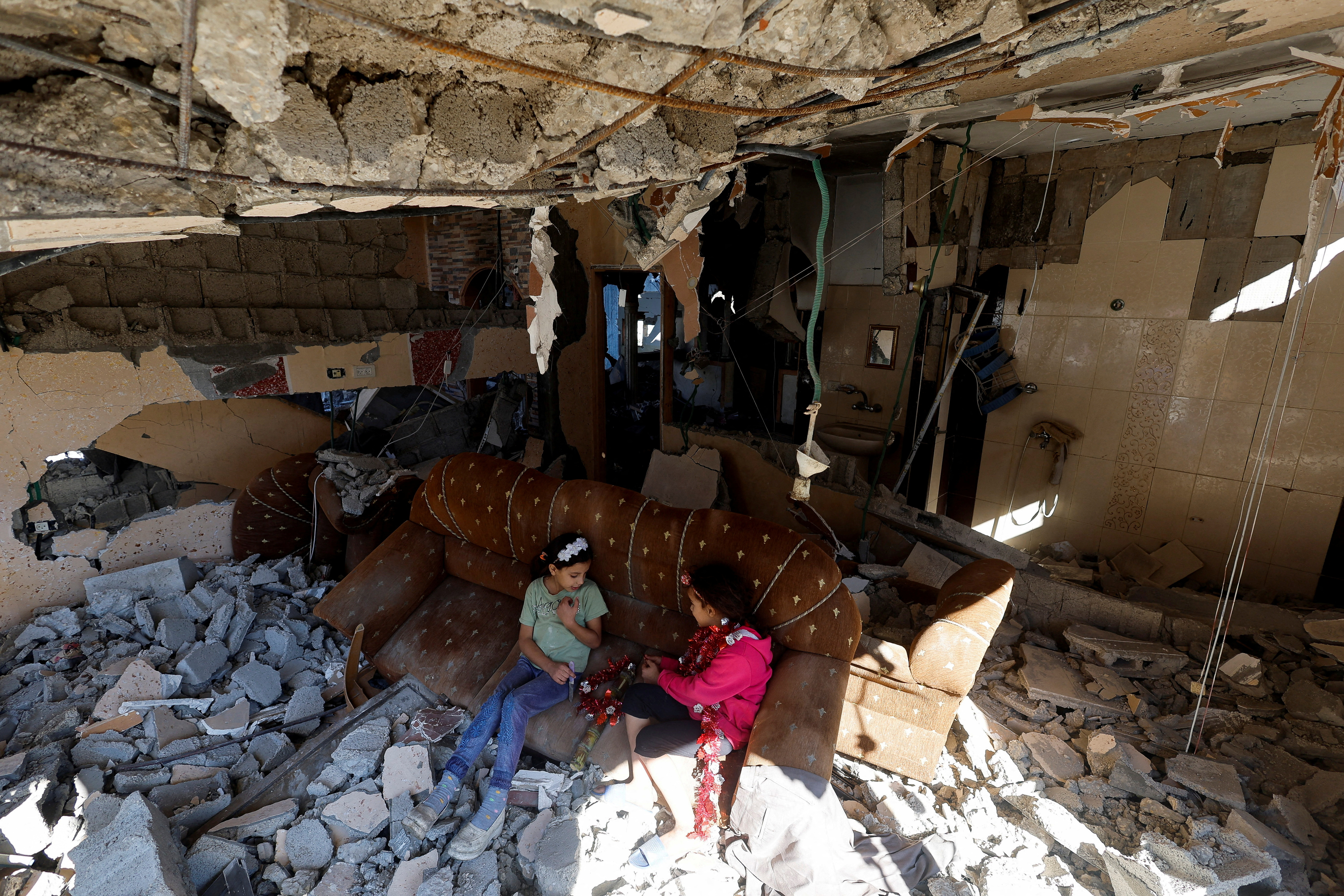 Palestinian girls sit on a couch at the remains of their house hit in Israeli strikes during the conflict, in Khan Younis
