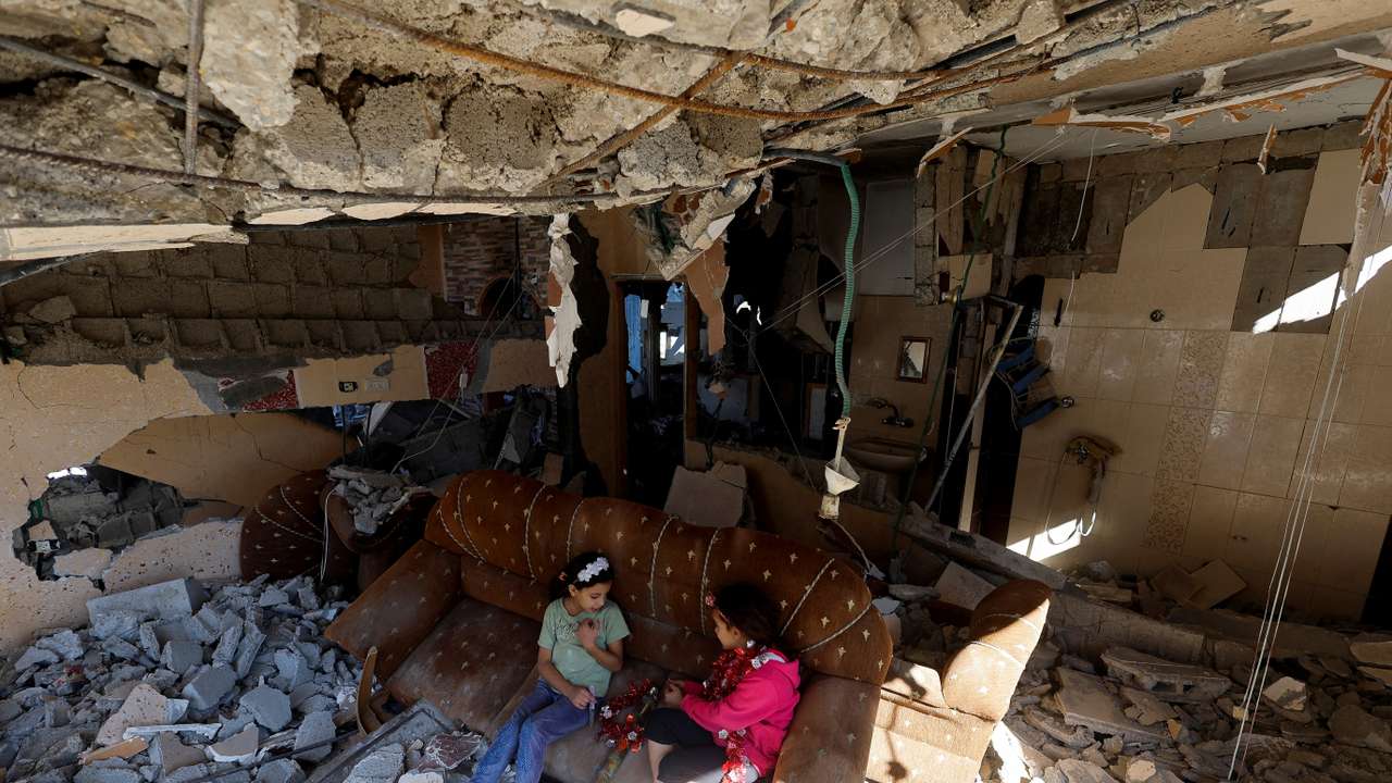 Palestinian girls sit on a couch at the remains of their house hit in Israeli strikes during the conflict, in Khan Younis