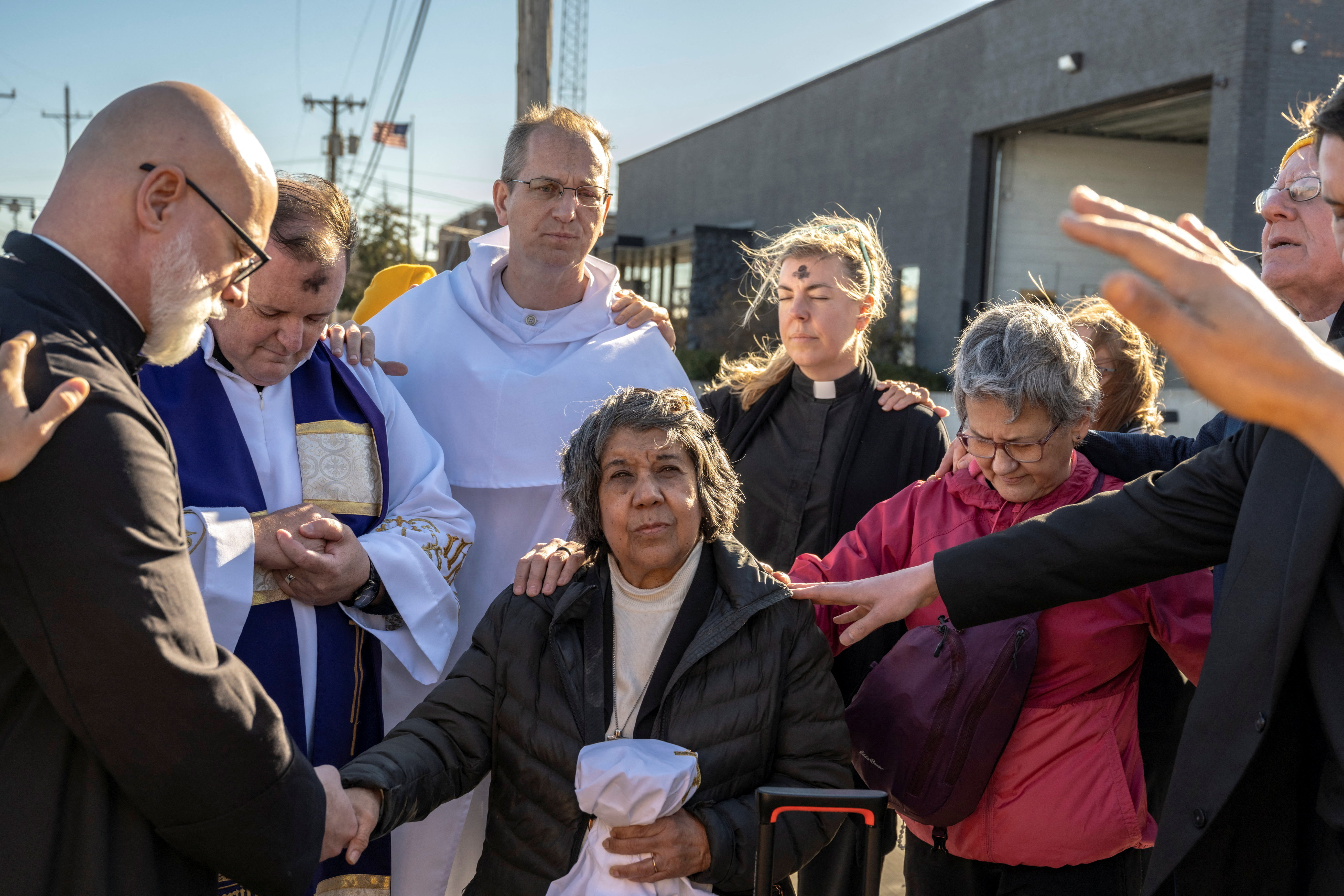 Faithful pray over two priests and a nun before they deliver communion and ashes to people detained in an immigration detention facility, in Broadview