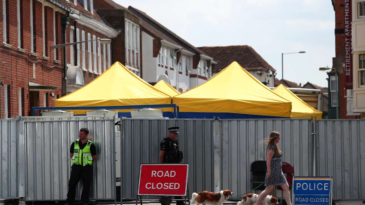FILE PHOTO: A woman walks her dogs past police officers stationed outside barriers blocking the street where Dawn Sturgess lived before dying after being exposed to a Novichok nerve agent, in Salisbury