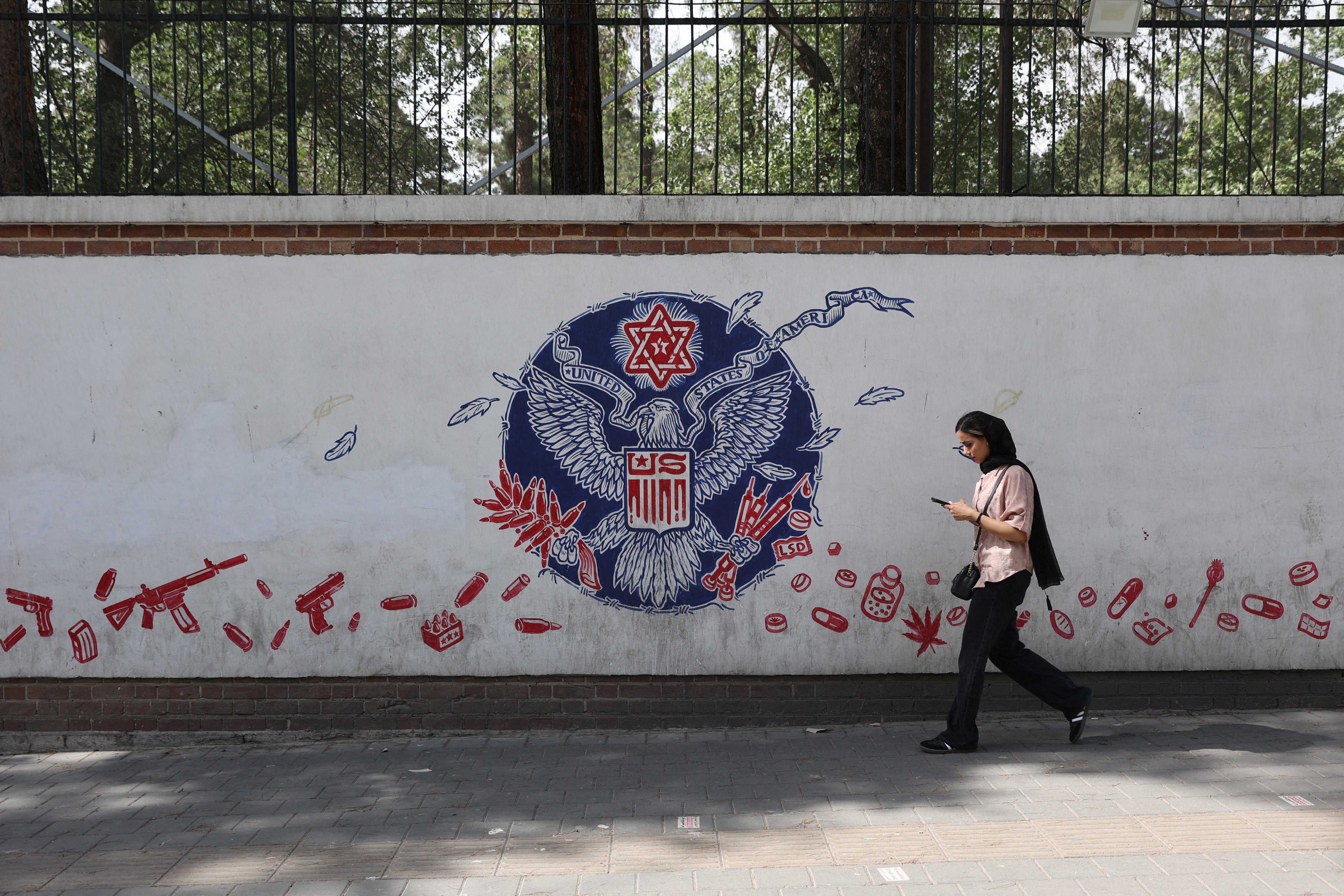 A woman walks past an anti-US mural on a street in Tehran