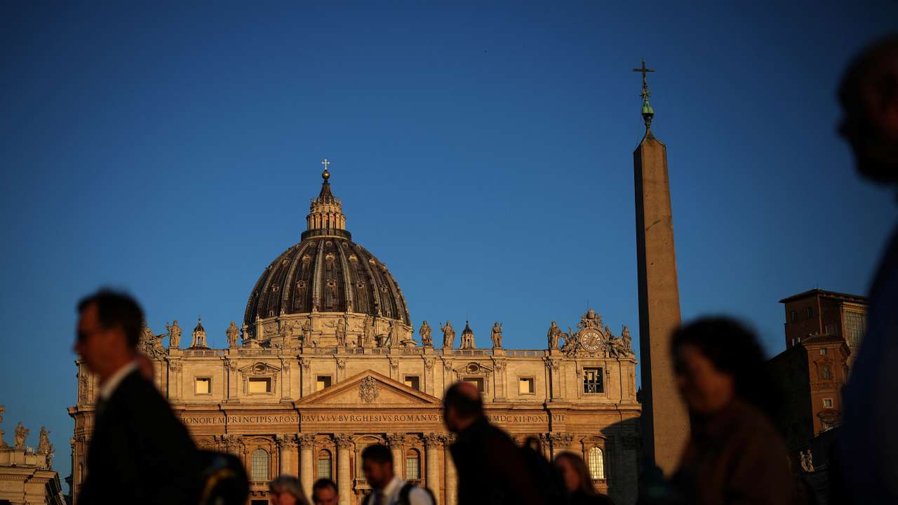 People walk in front of St. Peter's Basilica in St. Peter's Square ahead of the conclave, which will be held on May 7, at the Vatican
