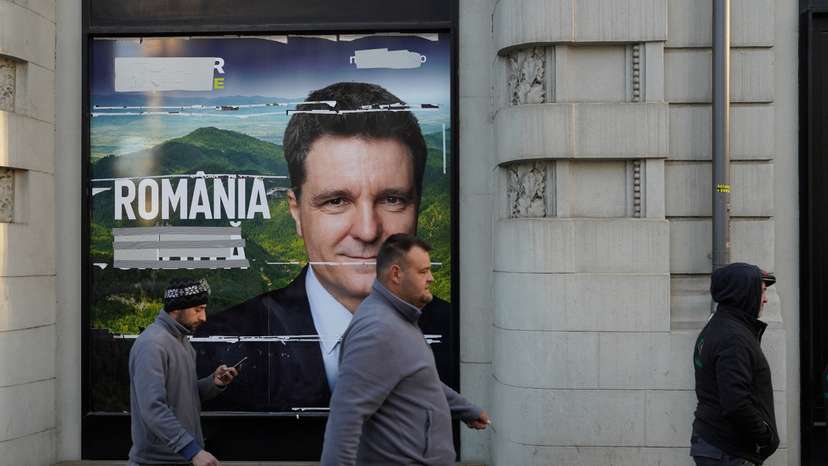 Three men pass by a poster of Nicusor Dan in Bucharest