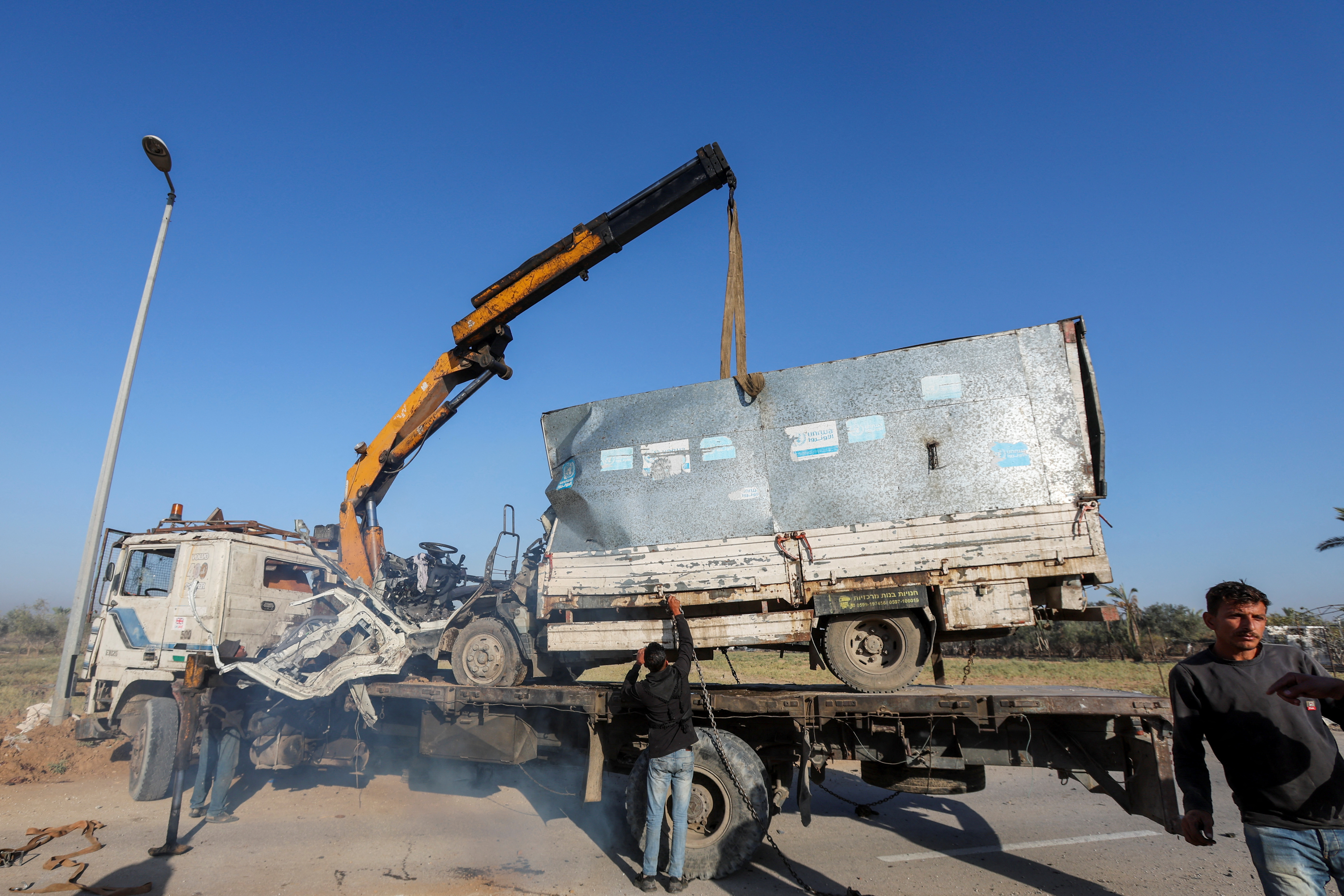 Palestinians work to remove an UNRWA-labelled vehicle after it was hit in an Israeli strike, according to Palestinian officials, amid the Israel-Hamas conflict, in Deir Al-Balah in the central Gaza Strip
