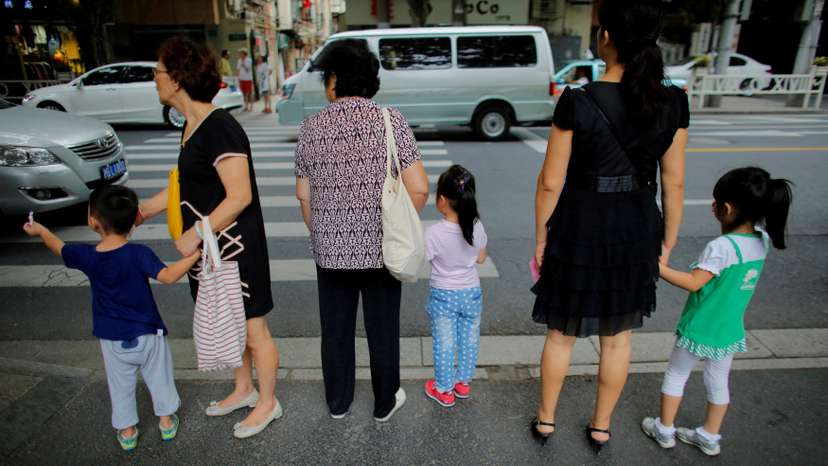 Women hold childrens' hands as they wait to cross a street after school in downtown Shanghai