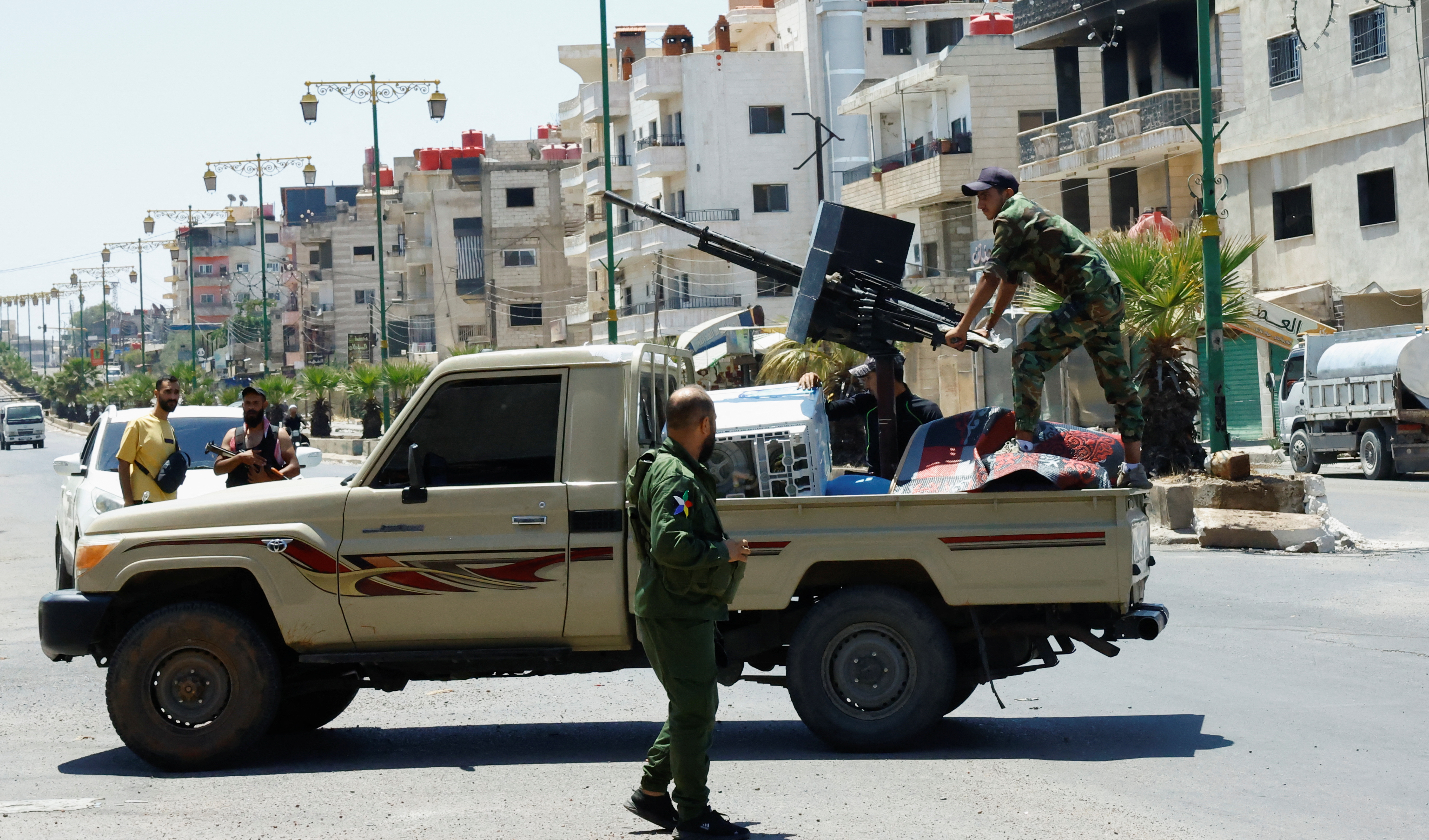A person wearing military clothing stands at the back of a vehicle, in Syria's predominantly Druze city of Sweida