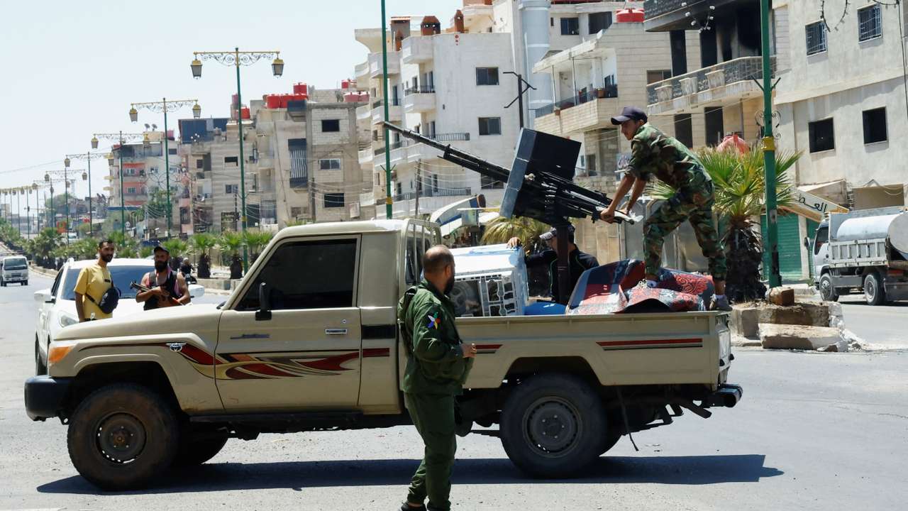A person wearing military clothing stands at the back of a vehicle, in Syria's predominantly Druze city of Sweida