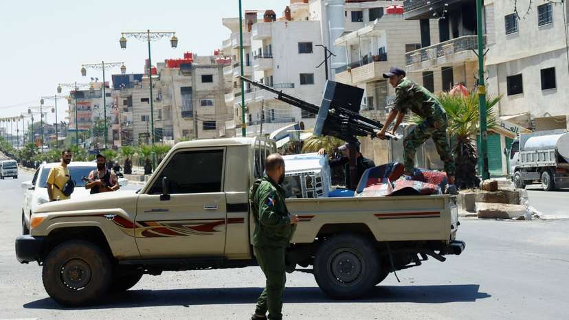 A person wearing military clothing stands at the back of a vehicle, in Syria's predominantly Druze city of Sweida