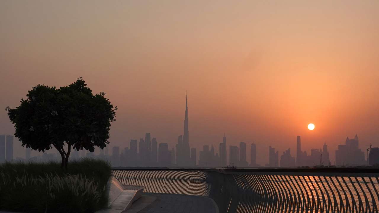 The Burj Khalifa building peaks through the skyline as the sun sets over Dubai