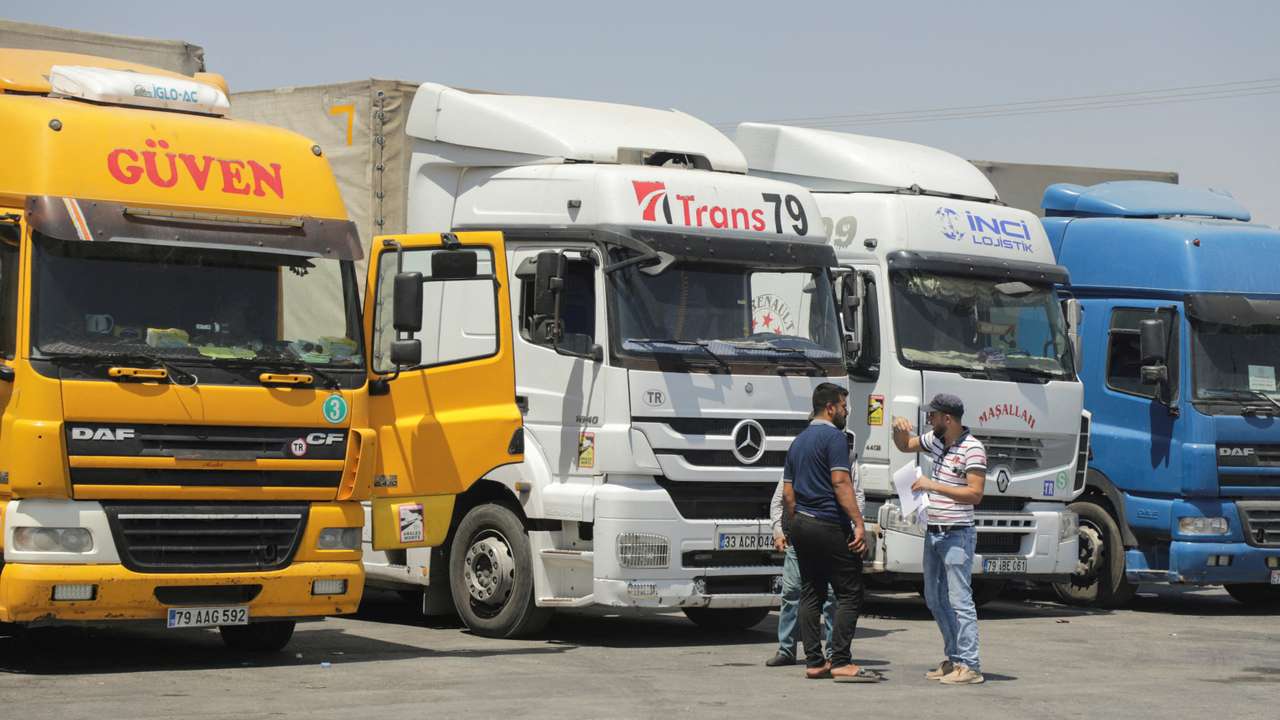 FILE PHOTO: People stand near trucks parked at Bab al-Salameh border crossing in Aleppo countryside