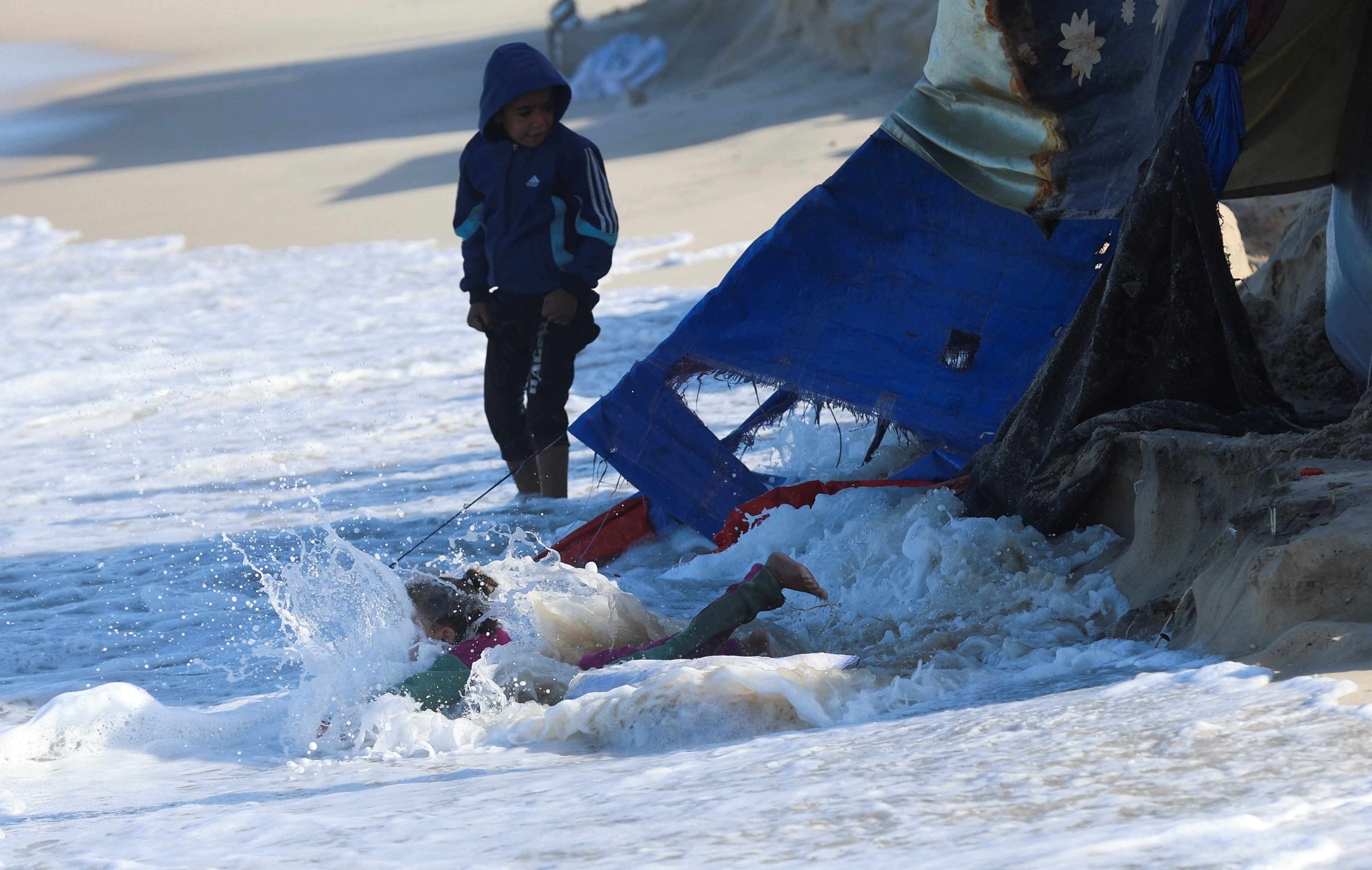 A child falls into the sea as Palestinians shelter in tents during a ceasefire between Israel and Hamas, in Khan Younis, southern Gaza Strip