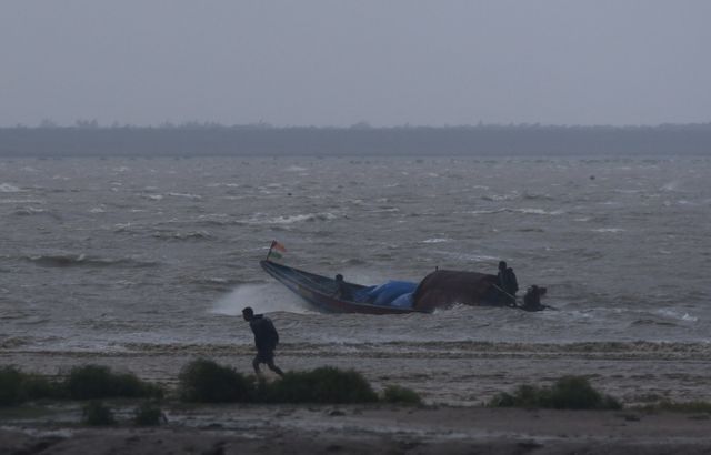 Fishermen attempt to bring their boat back to shore during high tide before Cyclone Dana makes landfall, in Odisha