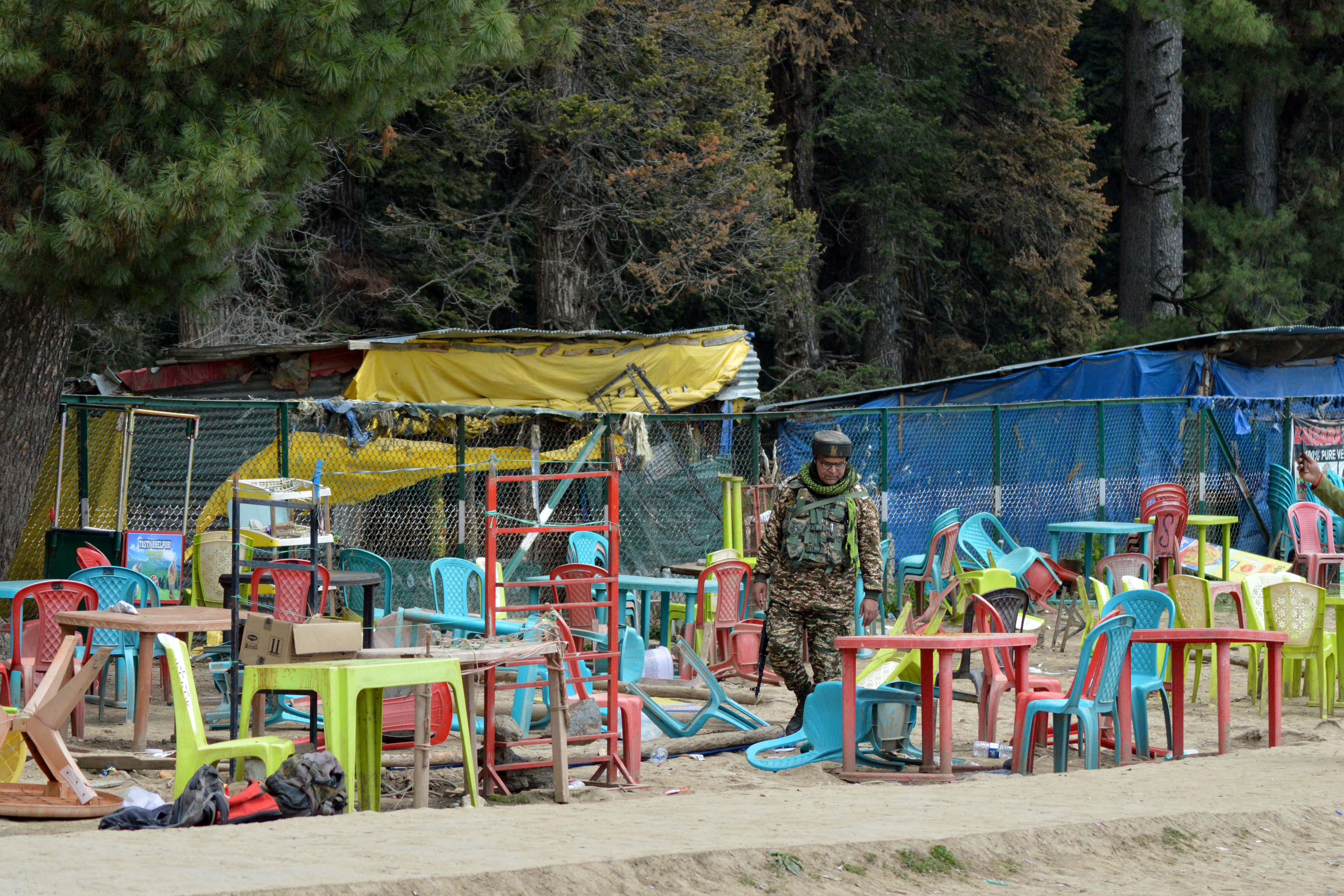 An Indian security force personnel walks amid toppled chairs and tables at the site of a suspected militant attack on tourists in Baisaran