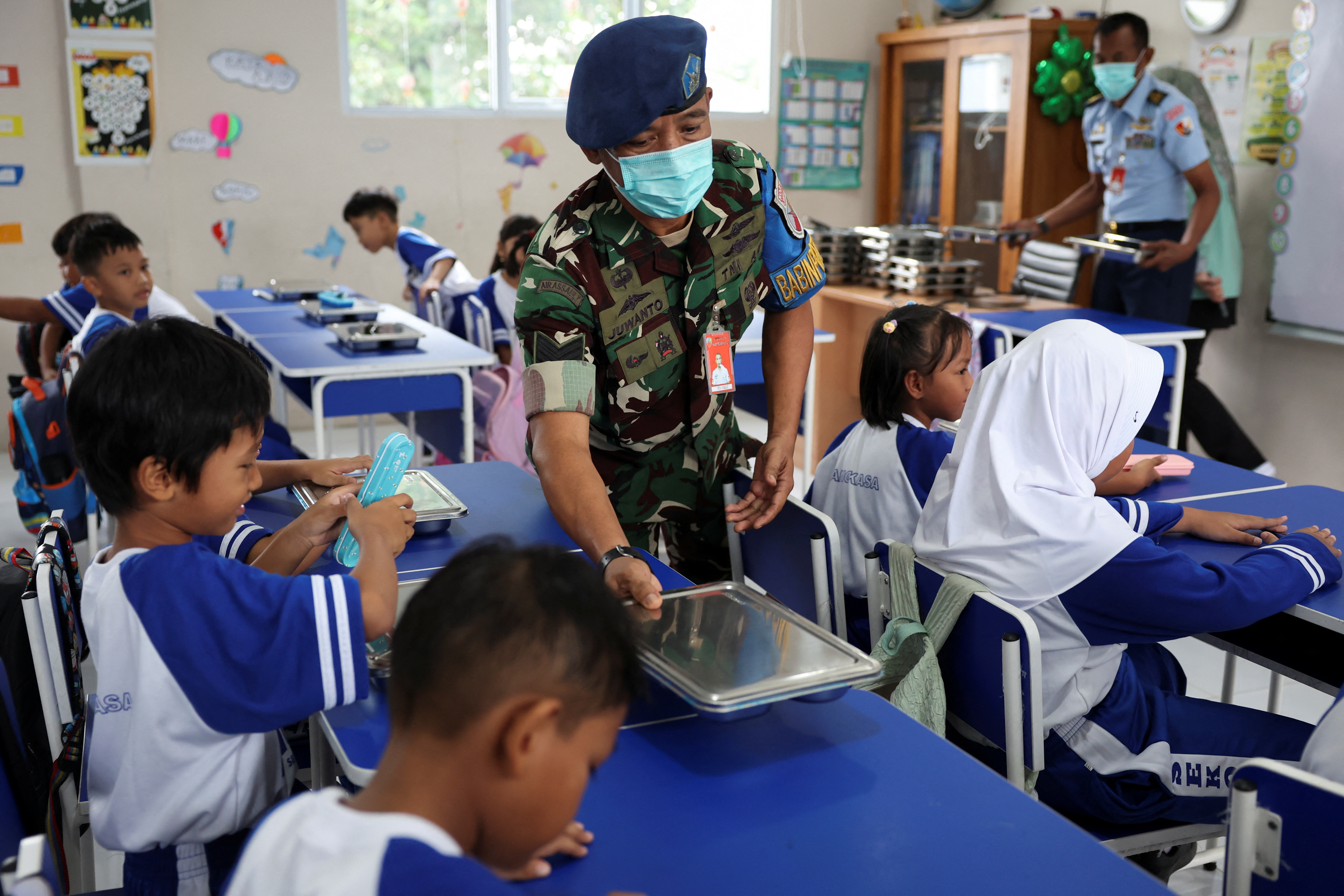 Indonesian Air Force personnel Juwanto offers a meal box to a student at the elementary school Angkasa 5 in Jakarta