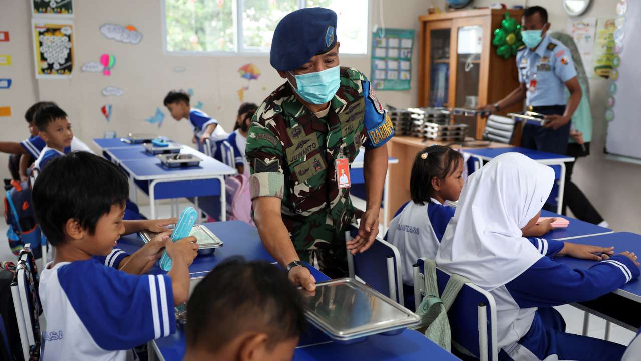 Indonesian Air Force personnel Juwanto offers a meal box to a student at the elementary school Angkasa 5 in Jakarta