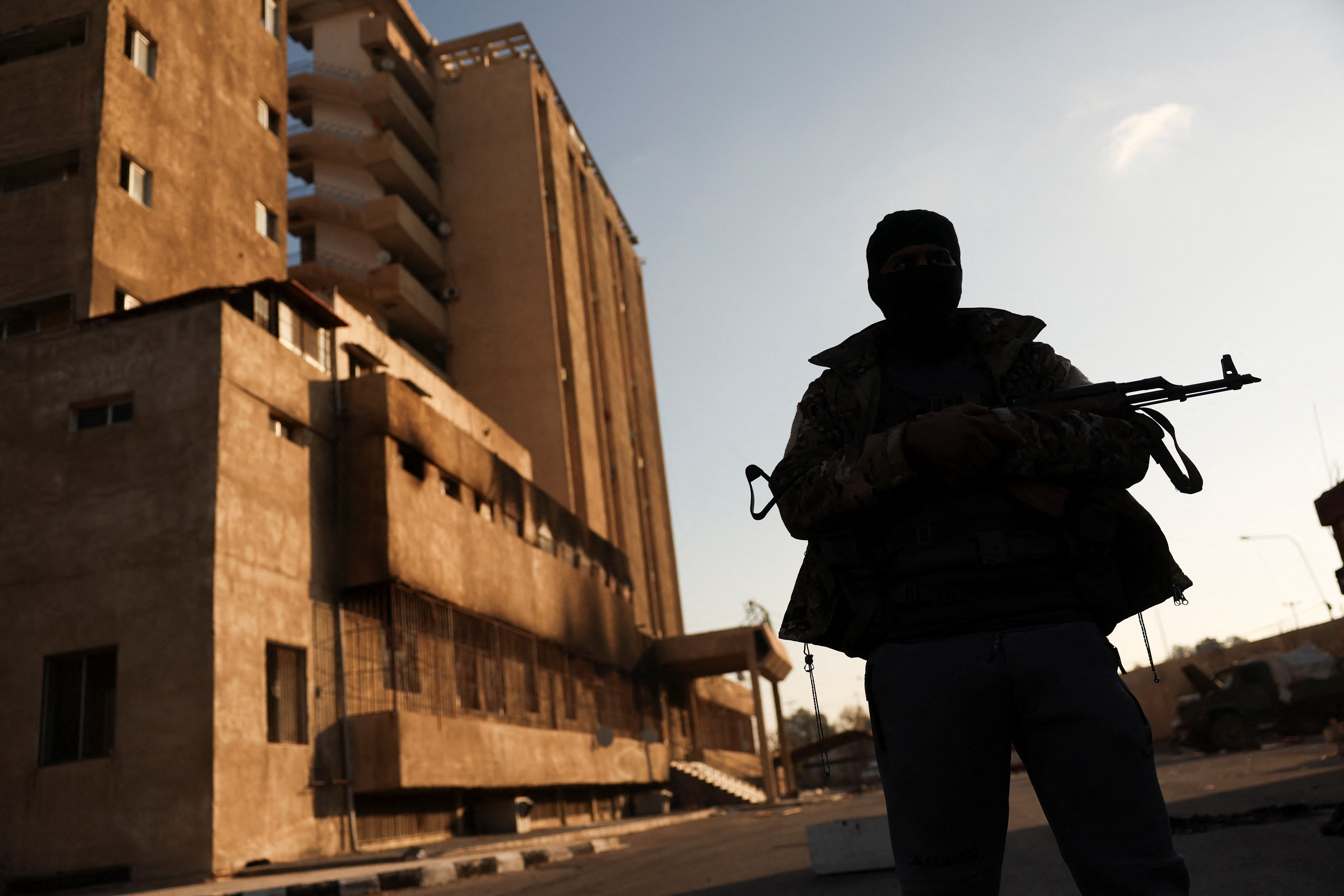 A fighter with Hayat Tahrir al-Sham (HTS) stands outside the Palestine Branch security complex in Damascus, Syria