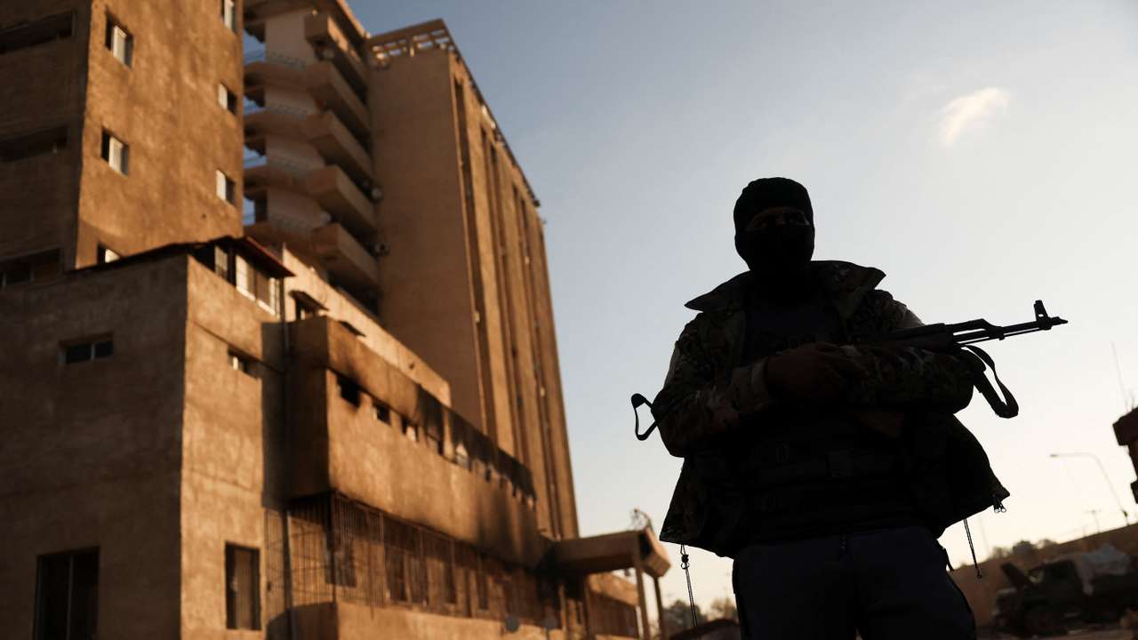 A fighter with Hayat Tahrir al-Sham (HTS) stands outside the Palestine Branch security complex in Damascus, Syria