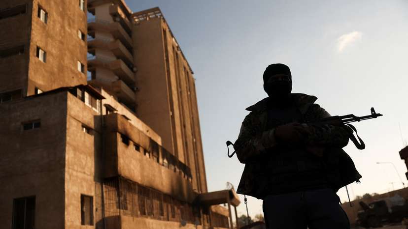 A fighter with Hayat Tahrir al-Sham (HTS) stands outside the Palestine Branch security complex in Damascus, Syria