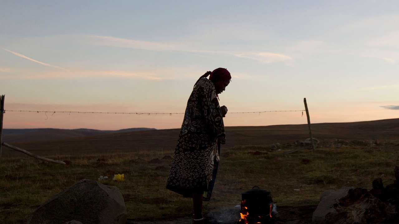A woman warms water on an open fire near the home of former South African President Nelson Mandela's house in Qunu