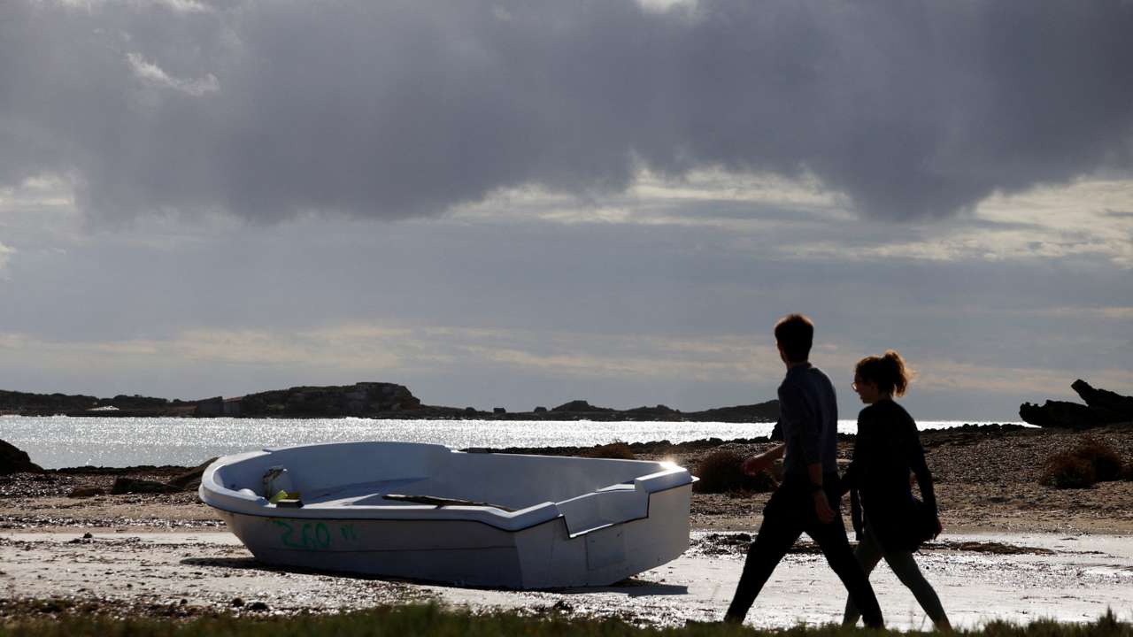 FILE PHOTO: People walk next to a discarded boat used by migrants to reach Mallorca rests on Es Caragol beach in the south of the Balearic island, in Santanyi