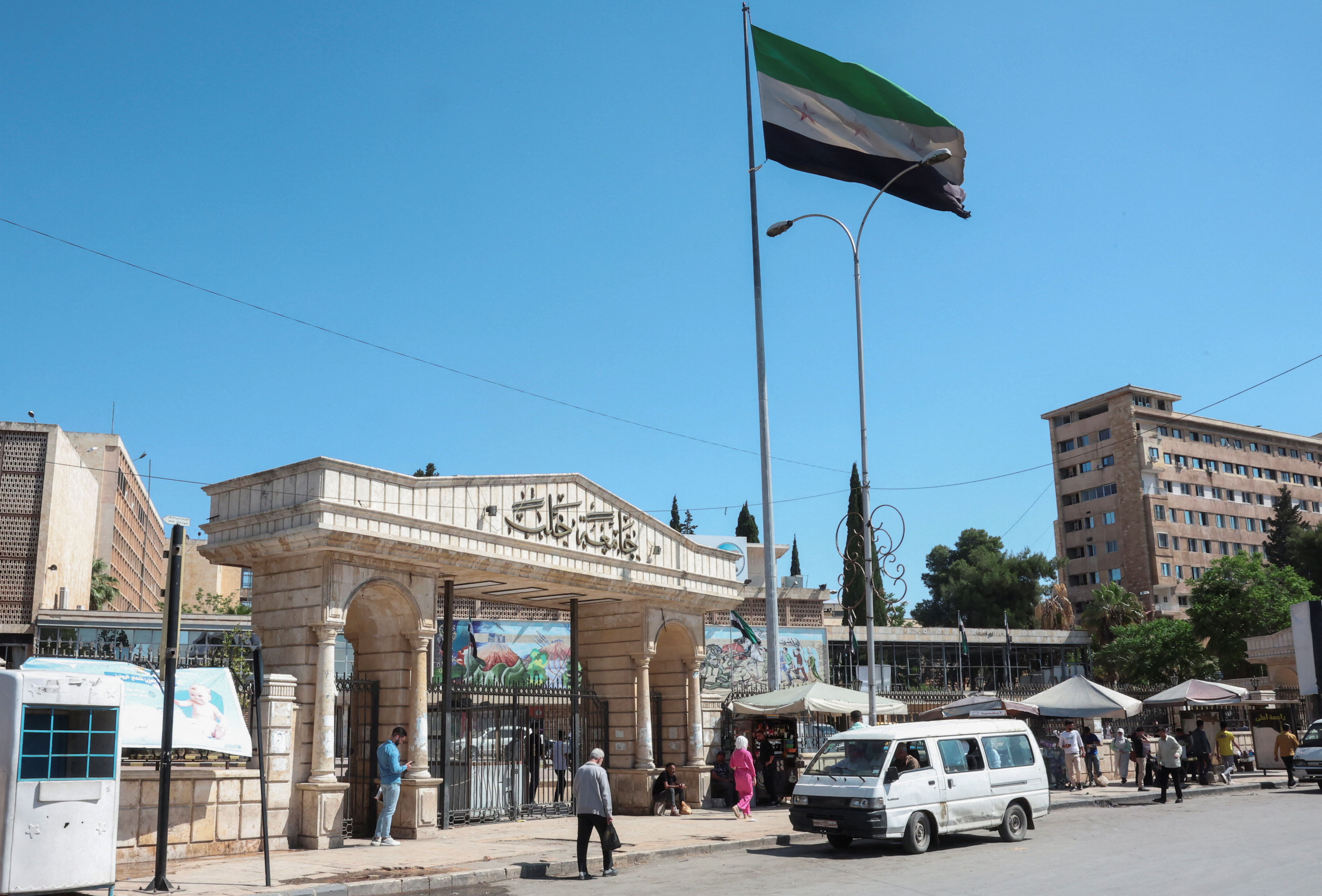 People walk near the Syrian flag, as U.S. President Donald Trump announced that he would order the lifting of sanctions on Syria, in Aleppo