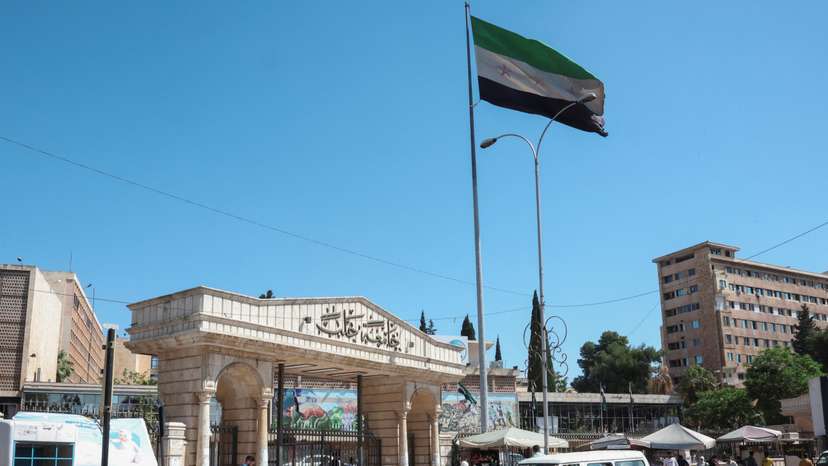 People walk near the Syrian flag, as U.S. President Donald Trump announced that he would order the lifting of sanctions on Syria, in Aleppo