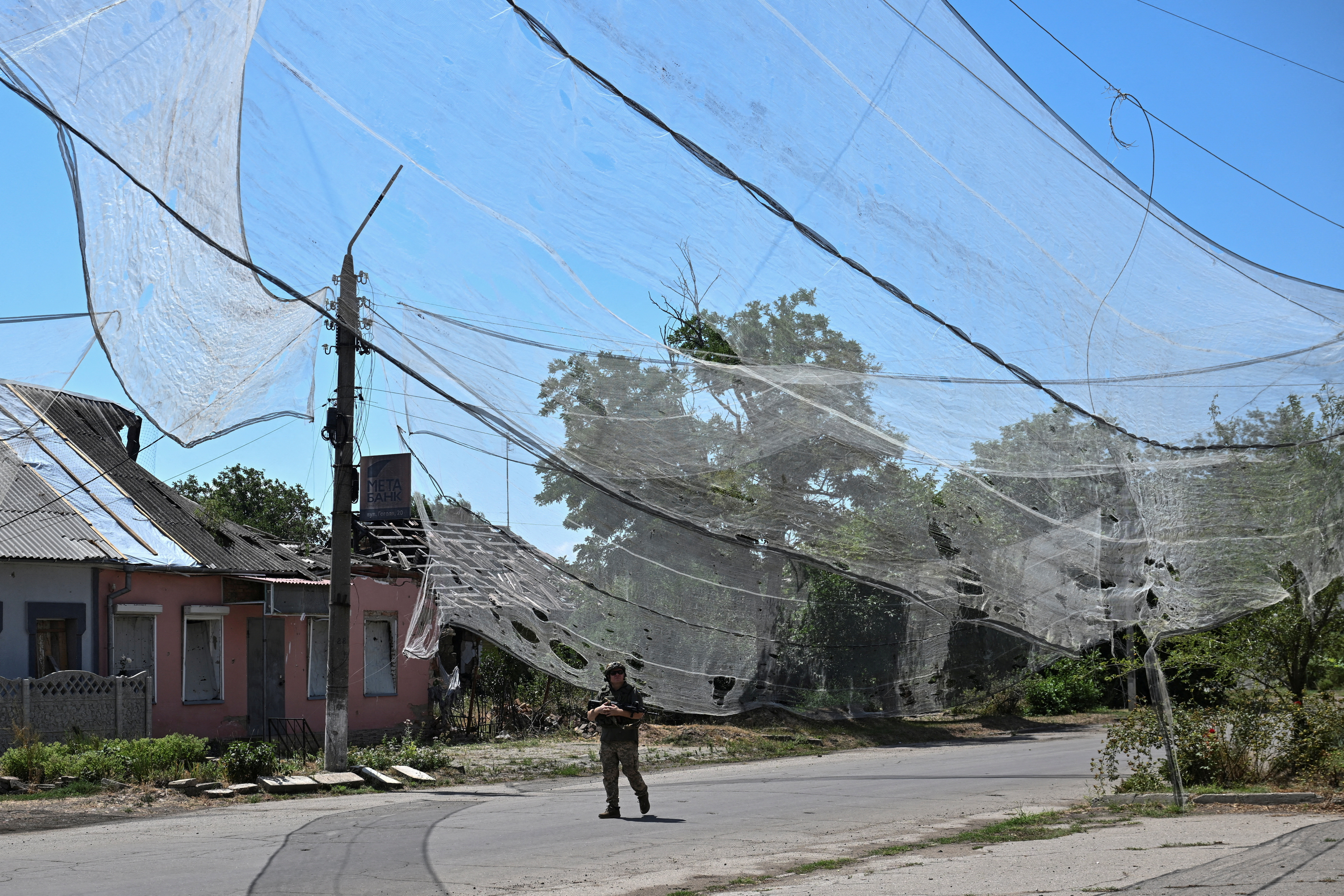Ukrainian service member walks on a street protected with anti-drone nets in the frontline town Orikhiv