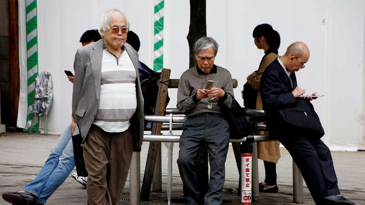An elderly man uses a mobile phone in front a station in Tokyo