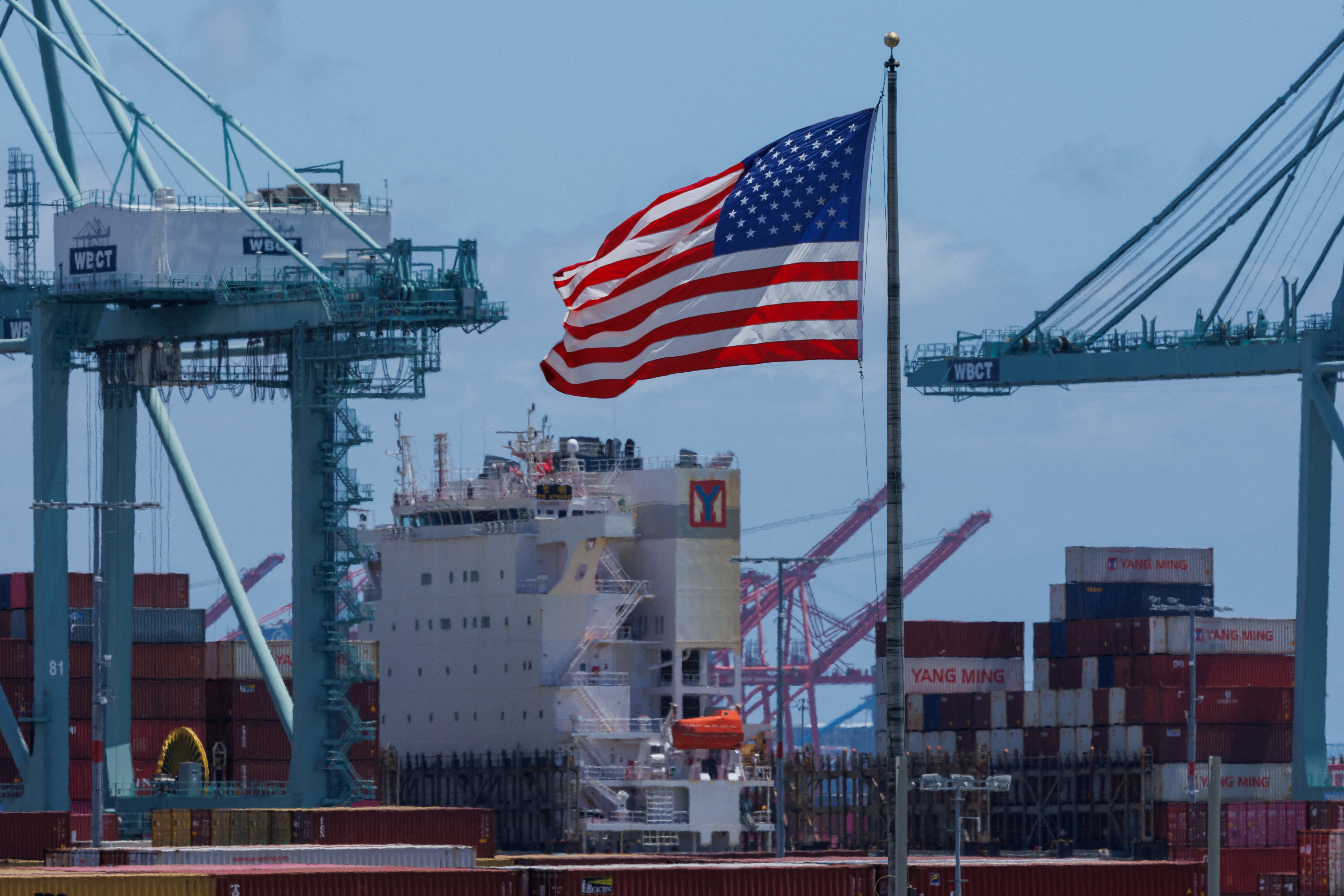 The American flag flutters near a ship at Port of Los Angeles