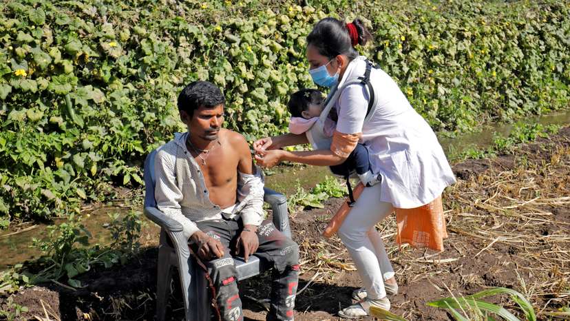FILE PHOTO: Asmita Koladiya carrying her eight-month-old daughter Jiyanshi Gaurang gives a dose of vaccine against COVID-19 to a villager in Lodhida